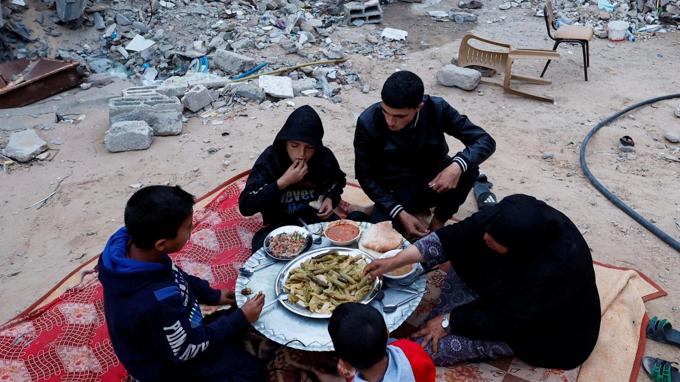 A Palestinian family eats their iftar meal they break their fast near the rubble of their destroyed house.