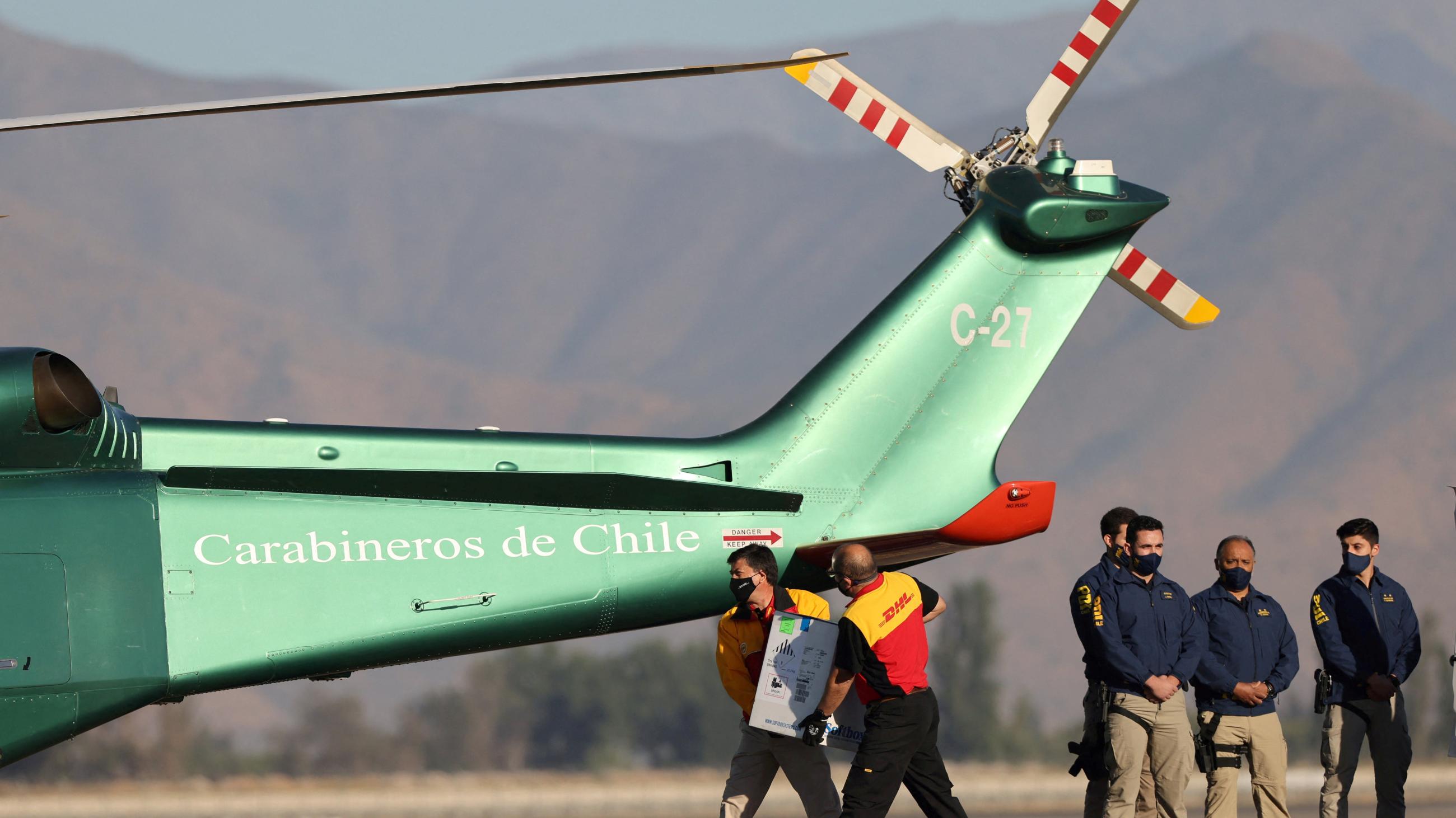 Workers carry a batch of the Pfizer-BioNTech COVID-19 vaccine to a helicopter.