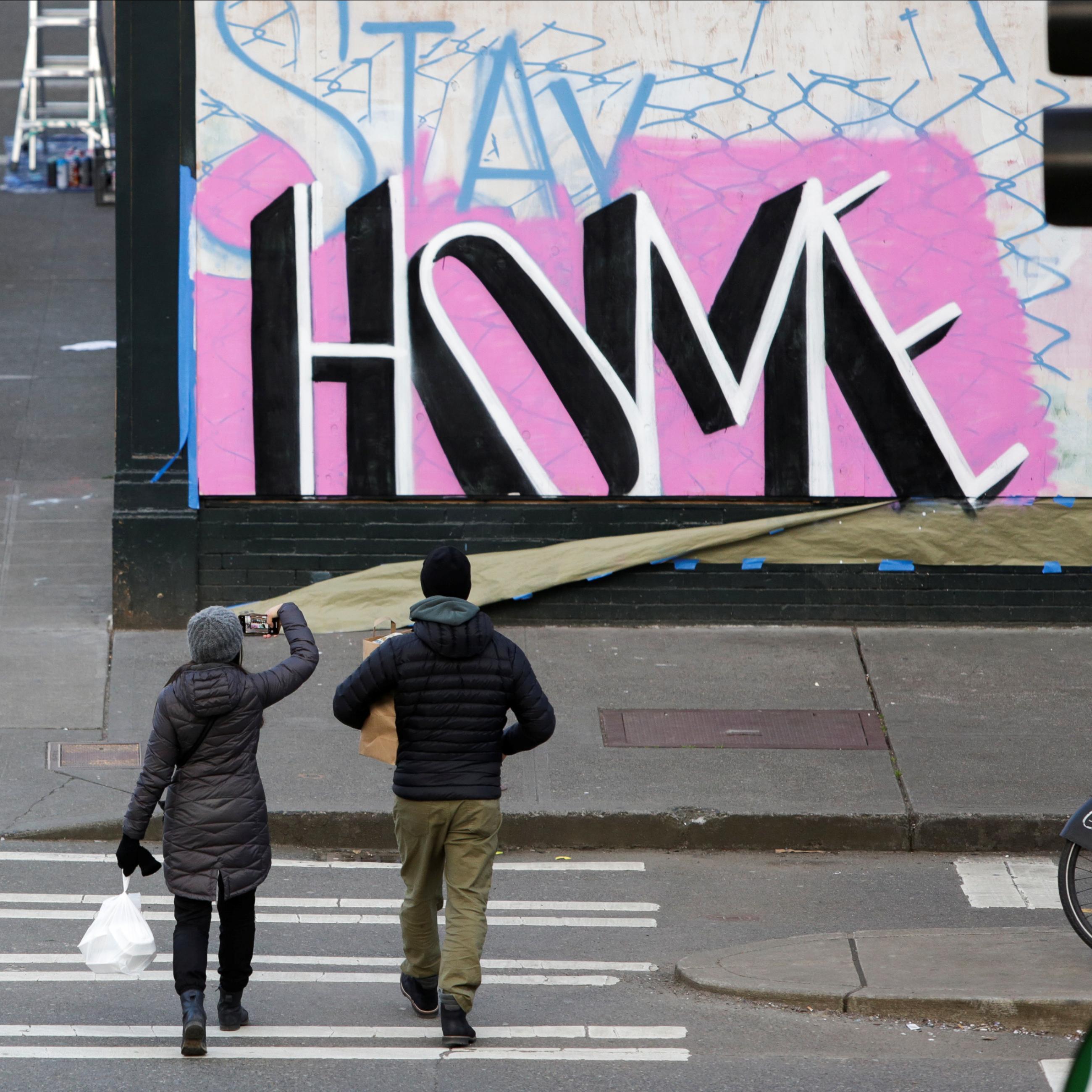 A couple totess take out food as they walk near street art with the message "stay home," on April 2, 2020, the same day that Washington Governor Jay Inslee extended a stay-home order to slow the spread of COVID-19 in Seattle, Washington.