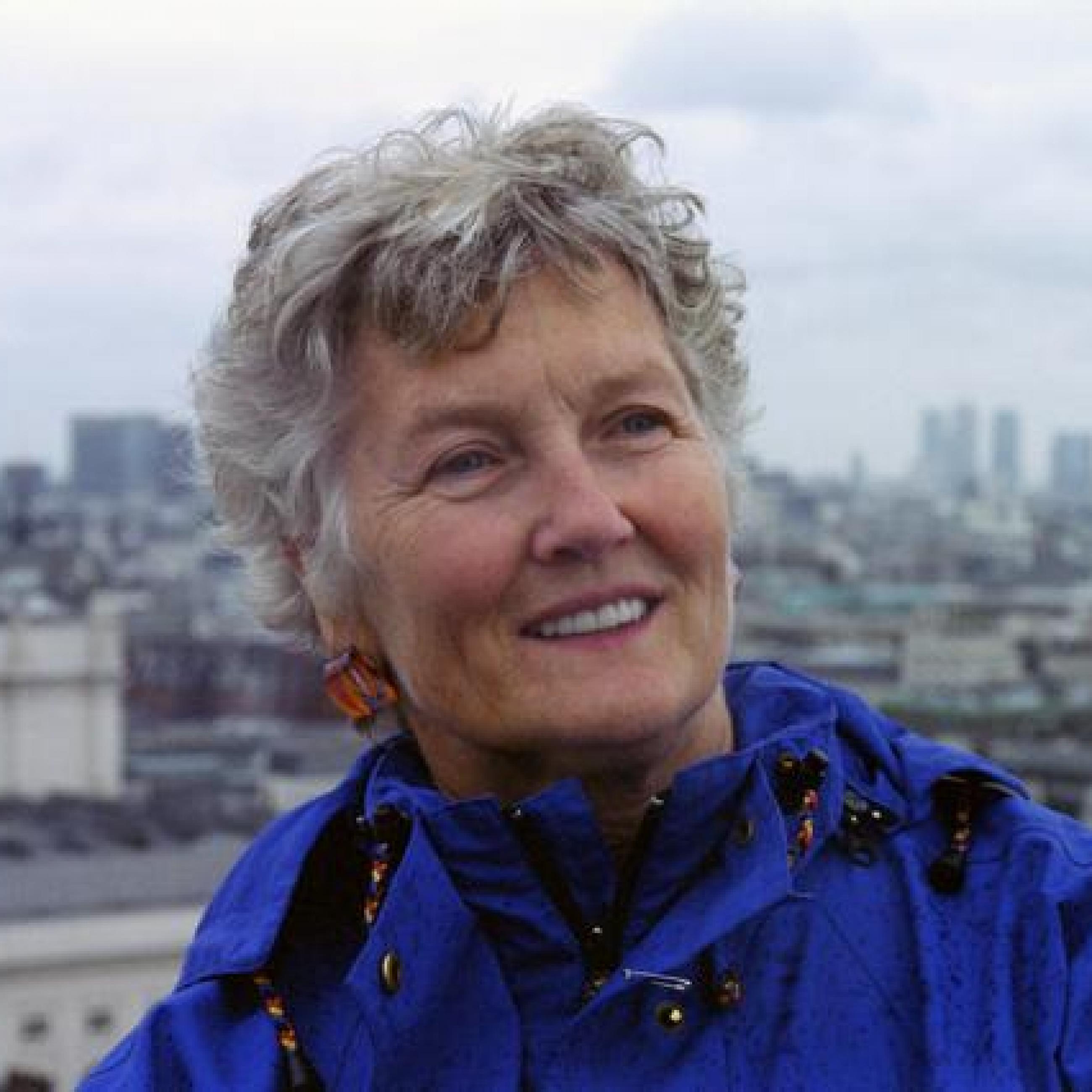 Peggy Seeger smiling with the skyline of Manchester, England in the background.