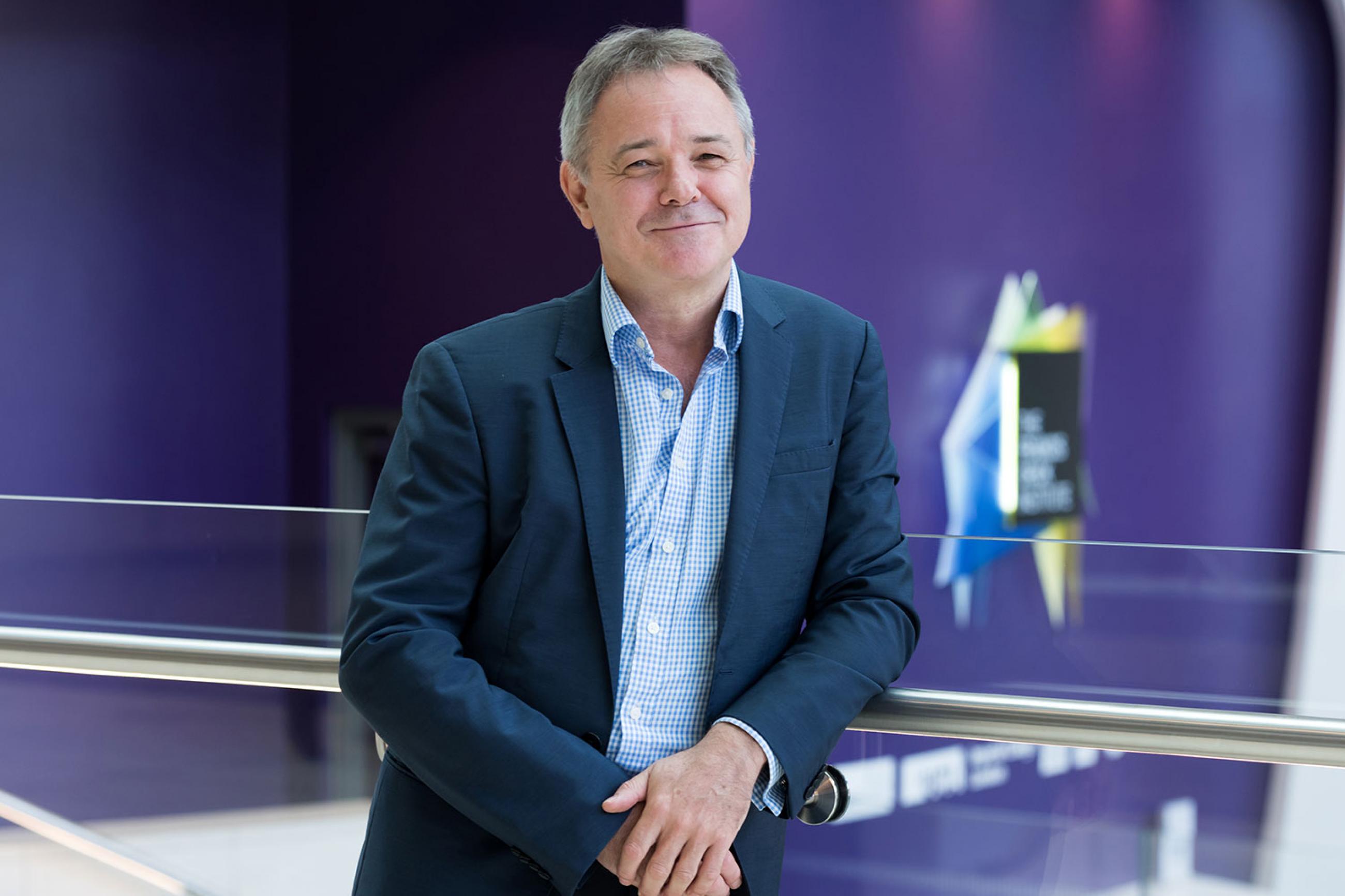 Jeremy Farrar, Director of the Wellcome Trust. The picture shows Farrar wearing a blue shirt and blazer, smiling as he leans on sleek railing and standing out against a highly bokeh background. FRANCIS CRICK INSTITUTE/Dave Guttridge
