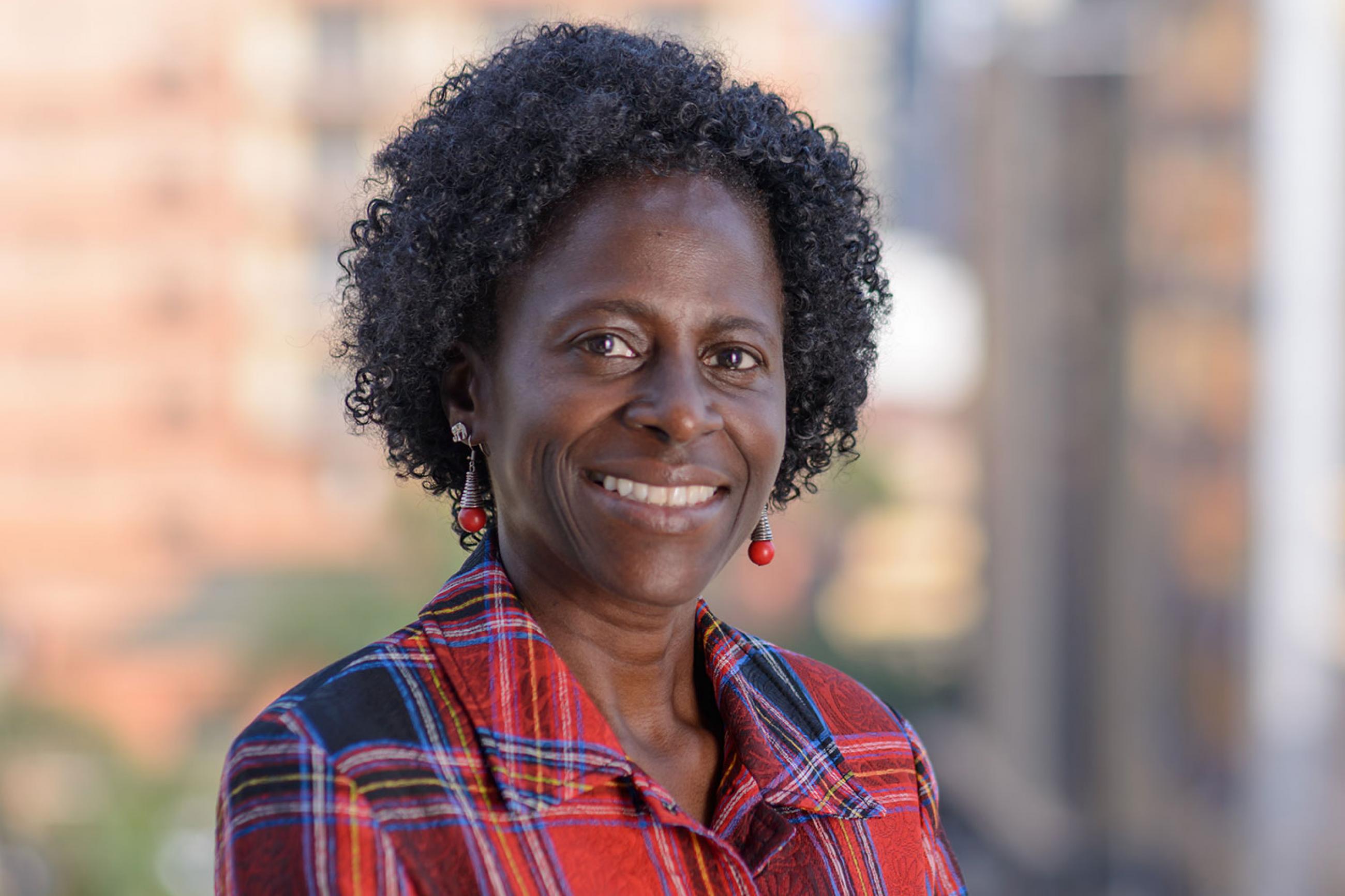 Picture shows Olive Kobusingye, Executive Director, Injury Control Center at Makerere Medical School in Kampala, Uganda. She is looking at the camera against a bright, blurred out background wearing a red-and-blue shirt in this posed shot. 