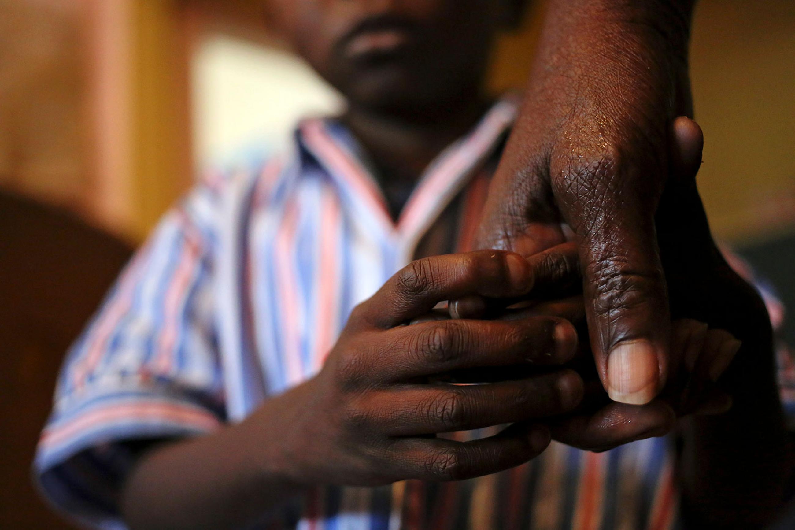 Nine-year-old Tumelo holds his grandmother's hand after taking his medication at Nkosi's Haven, south of Johannesburg, on November 28, 2014. Picture shows a large adult hand and the lower part of a child’s face in the background as his own hand grasps his grandmother’s. 