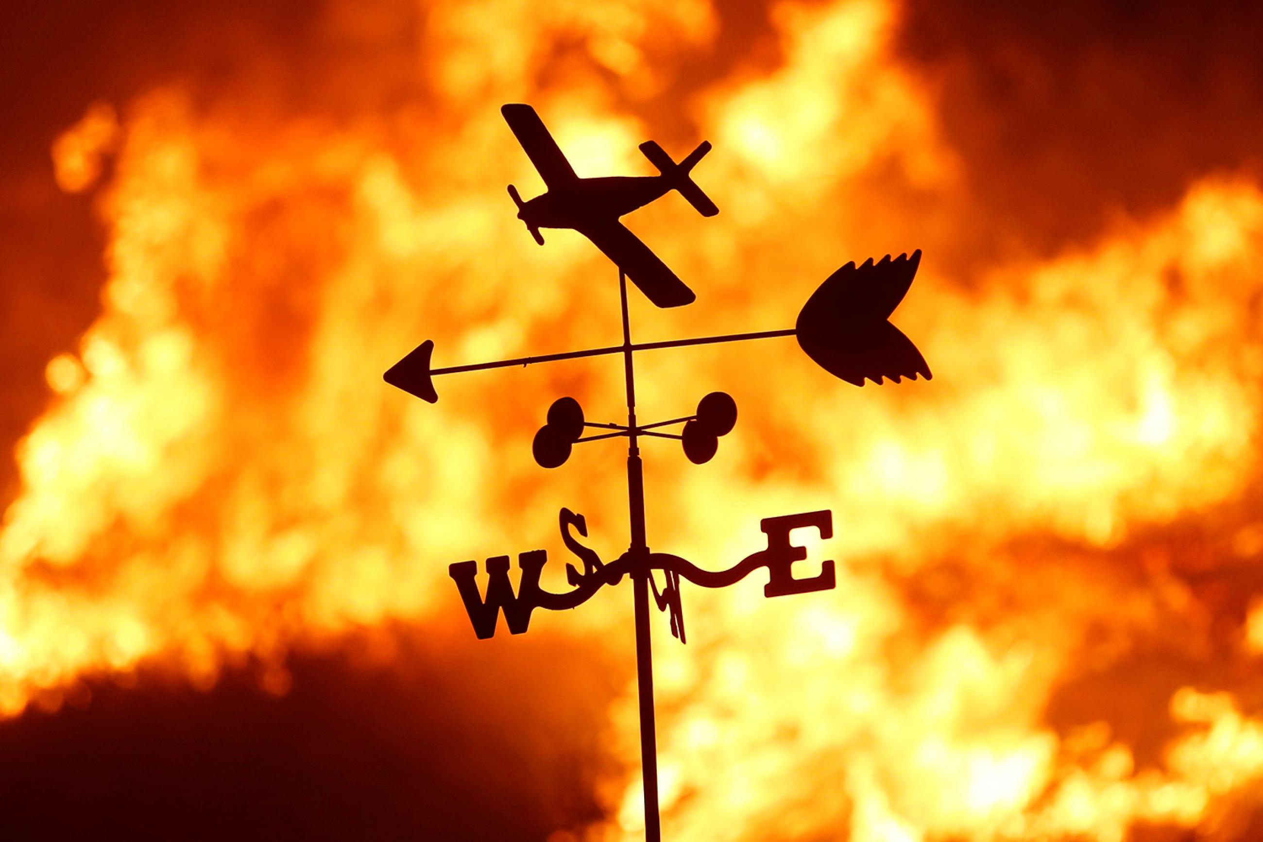 A weather vane is pictured on a ranch during the Creek Fire in the San Fernando Valley north of Los Angeles, in Sylmar, California on December 5, 2017. Picture shows a thin metal toy-like vain with a plane, and arrow and a “NESW” directional indicator silhouetted against a burning fire. REUTERS/Jonathan Alcorn