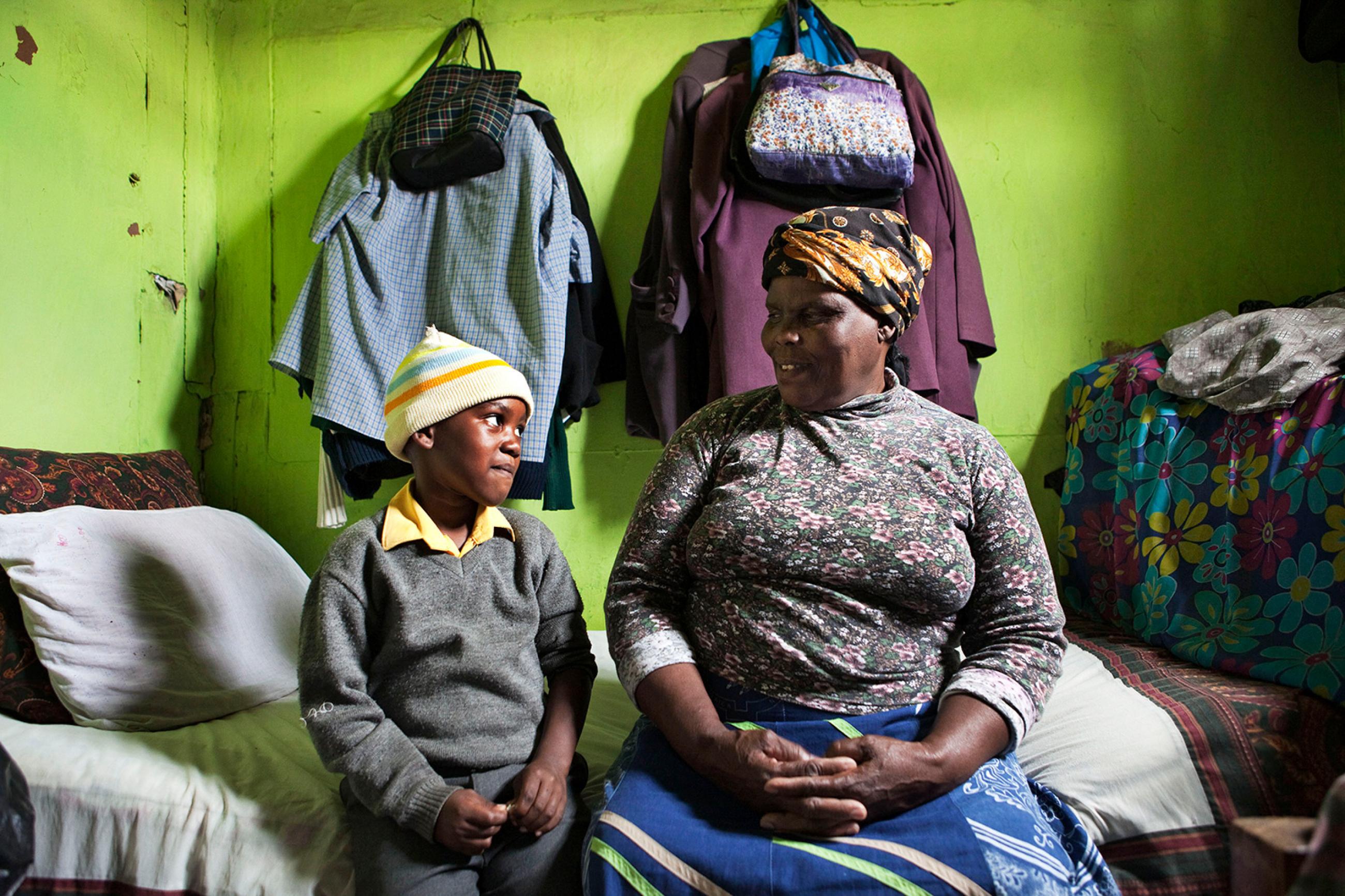 Two ends of the age spectrum: Thenjiwe Madzinga, 66, and grandson Thina Gxotelwa in a small room they share in Cape Town's Khayelitsha township on Feb. 23, 2010. Madzinga cares for five grandchildren. Picture shows the pair sitting on a bed in a small room with bright green walls. She is looking lovingly at him, and he is looking at her and smiling, perhaps embarrassed at the camera. REUTERS/Finbarr O'Reilly