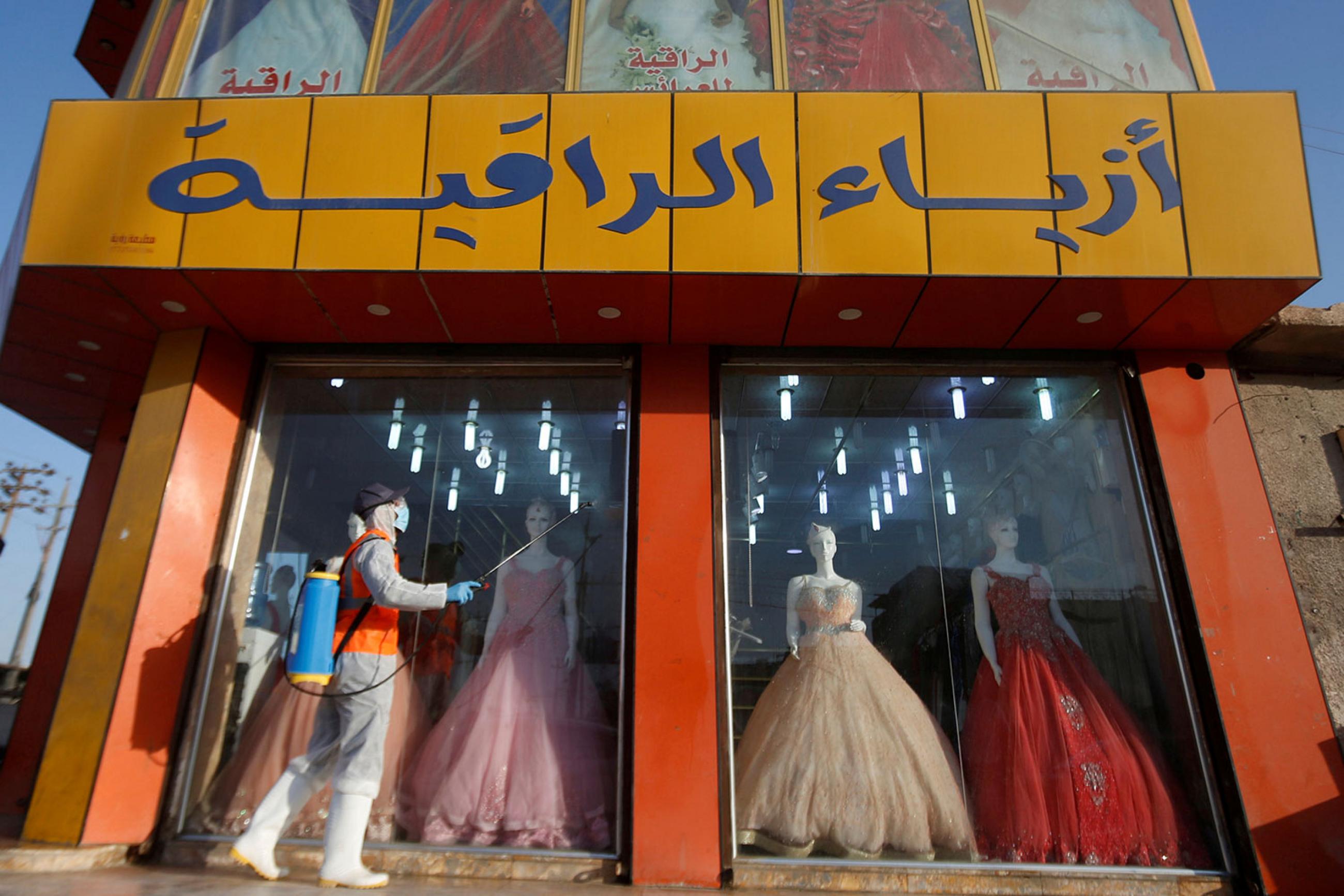 A worker in protective suit sprays disinfectants in front of a dress shop at popular market following the outbreak of the coronavirus in Basra, Iraq on March 10, 2020. This is an interesting photo showing a colorful dress shop with a worker walking by outside in protective gear spraying disinfectant. REUTERS/Essam al-Sudani 