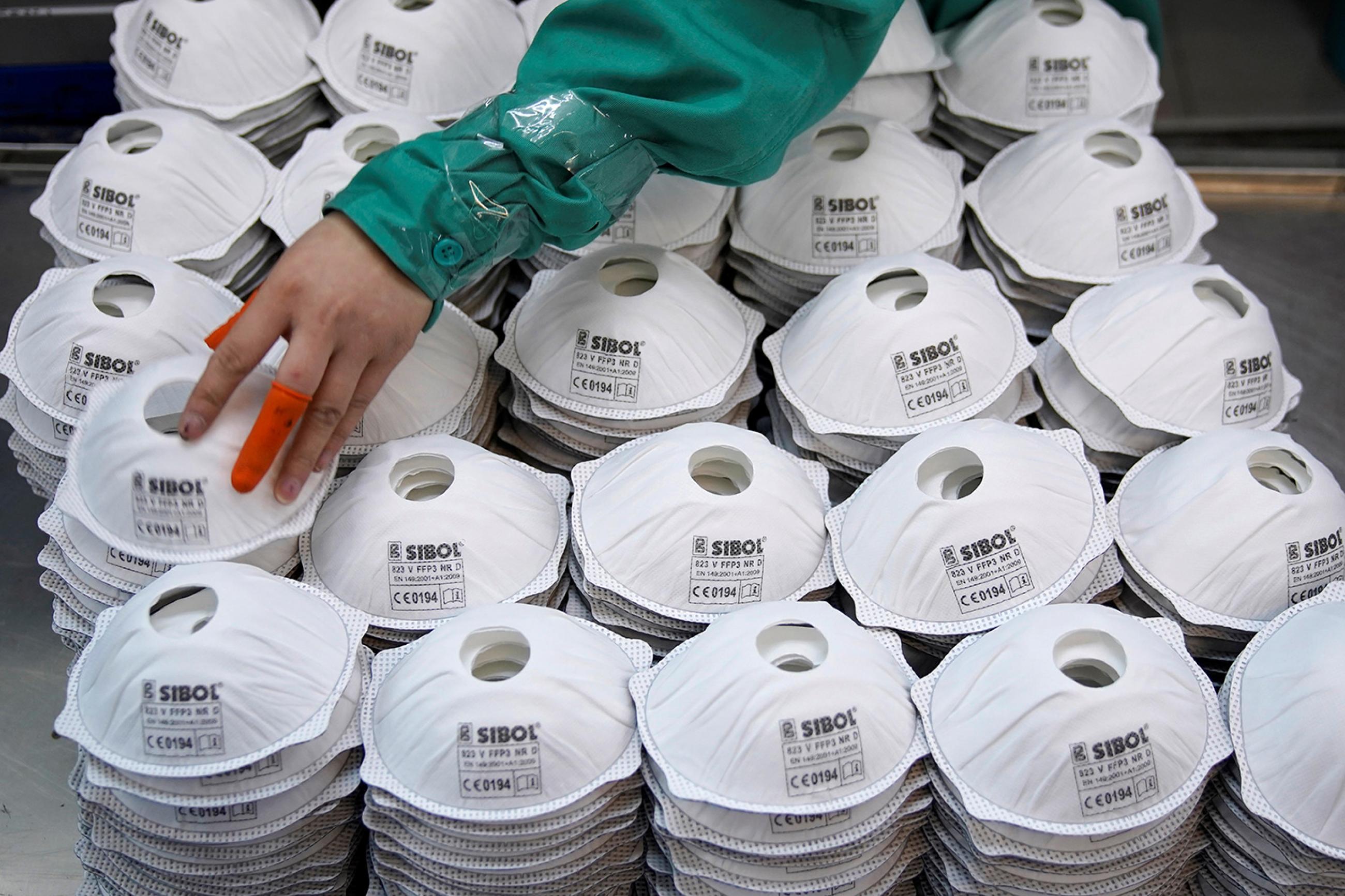 Masks are seen on a production line manufacturing masks at a factory in Shanghai, China January 31, 2020. New York City alone could face a shortage of millions of masks in the coming months. The image shows a human hand with two bright orange bandaids on the thumb and middle finger picking its way across a huge pile of masks. REUTERS/Aly Song