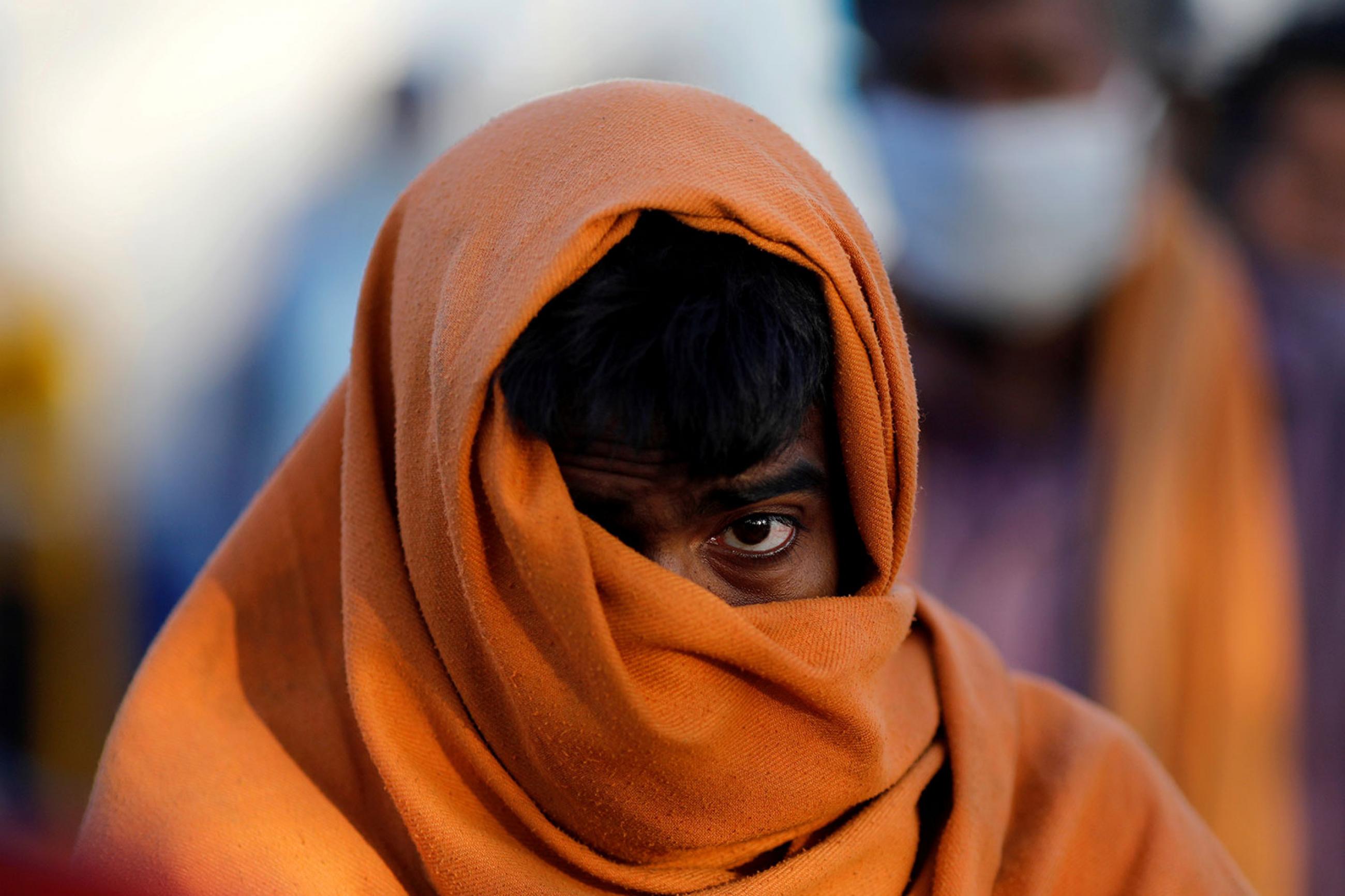 A homeless man stands in a queue as he waits for food during a 21-day nationwide lockdown to slow the spreading of the coronavirus disease (COVID-19) in New Delhi, India on April 3, 2020. The image is very striking showing the man with a large wrap around his head and mouth against a creamy, out of focus, colorful background. REUTERS/Adnan Abidi 