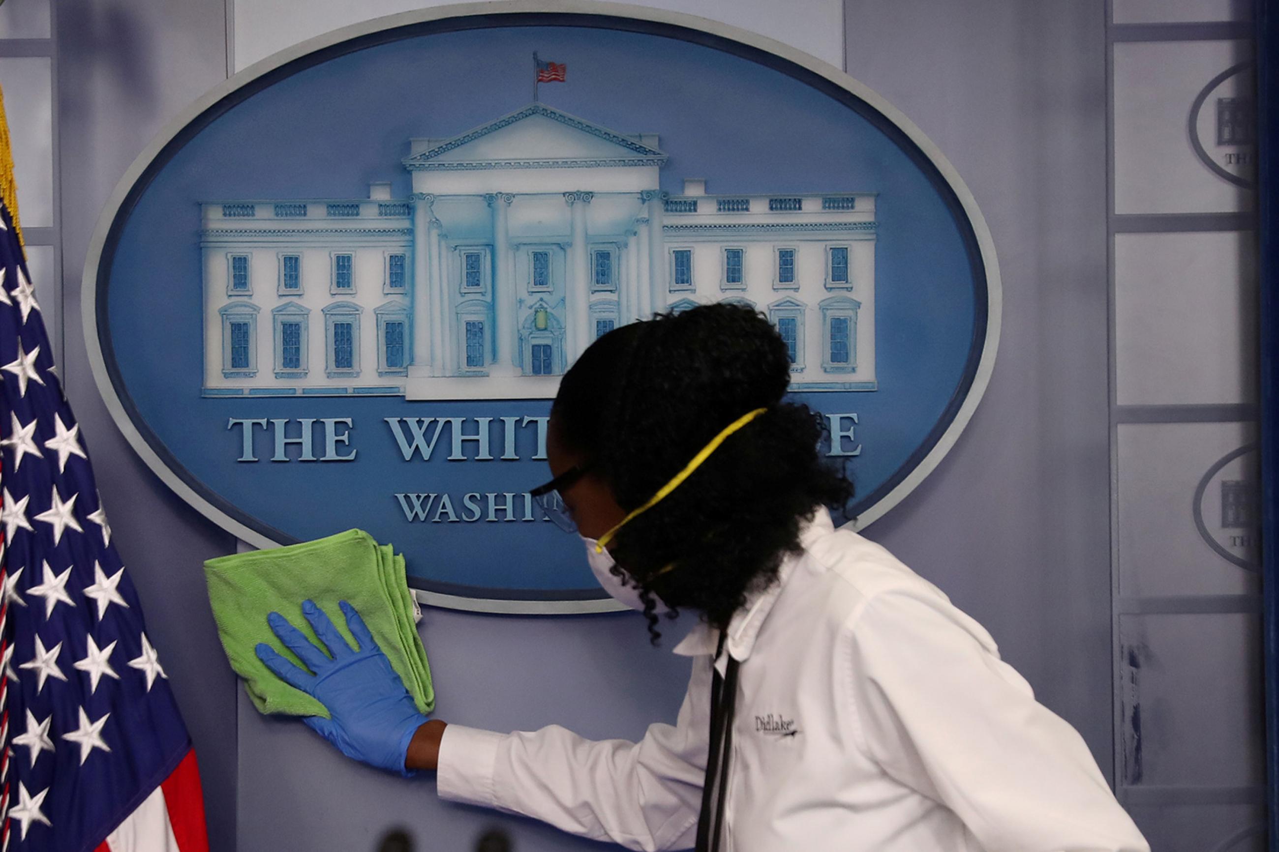 Workers clean the area around the podium before a coronavirus disease (COVID-19) outbreak task force press conference in the briefing room at the White House in Washington, D.C. on April 13, 2020. This is a striking image for its subject matter. It's a shot of the podium we don't normally see—empty of politicians and instead a worker in protective gear is cleaning the White House emblem. REUTERS/Leah Millis 