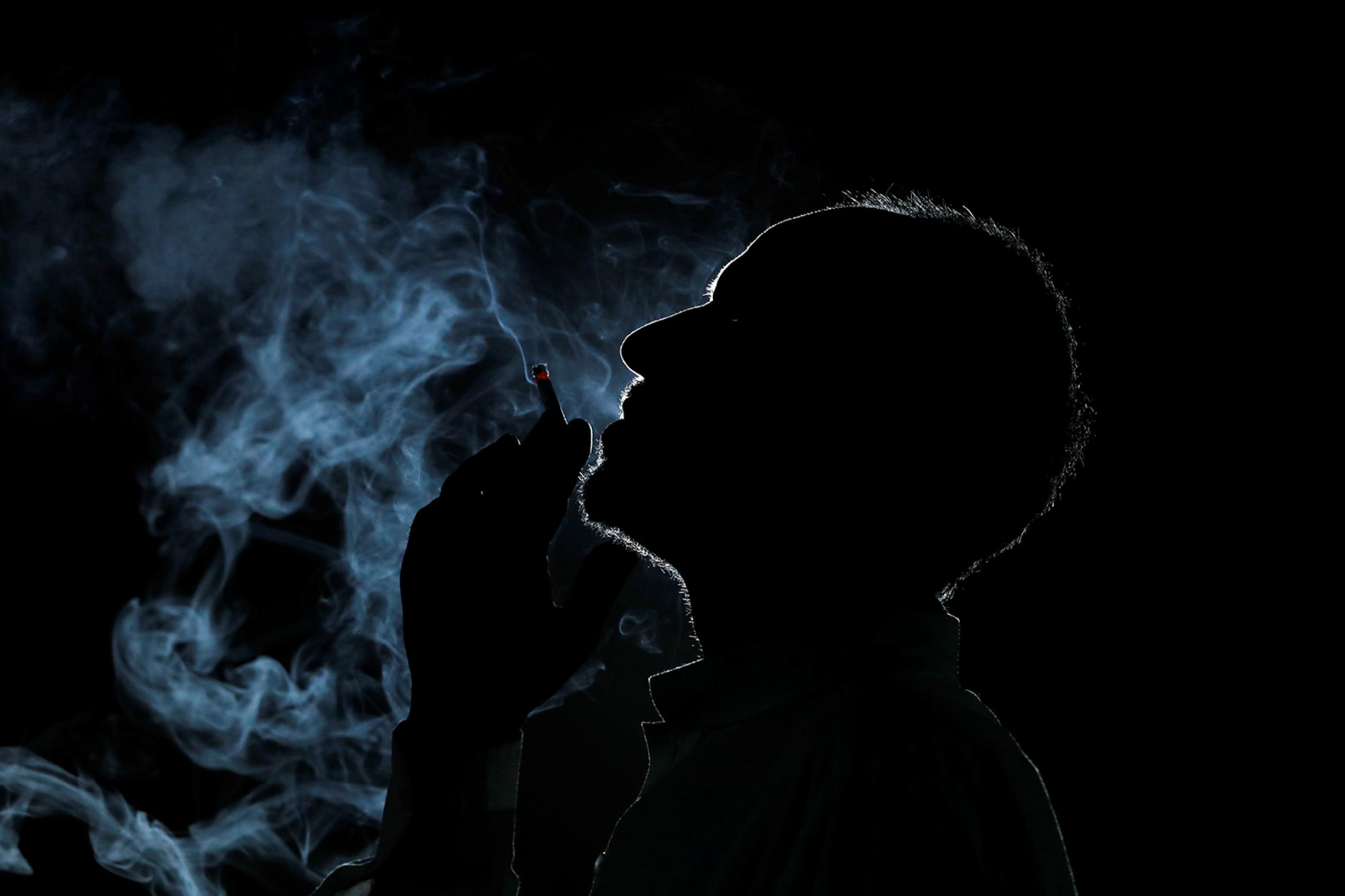 A man is seen in silhouette as he smokes a cigarette at his shop in Peshawar, Pakistan May 28, 2019. The image shows a dark silhouette of a man in profile smoking and filling the air around him with smoke. REUTERS/Fayaz Aziz