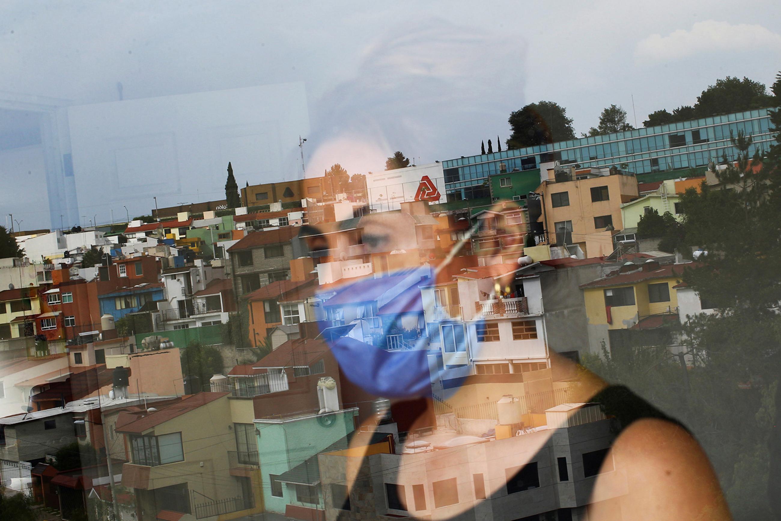 Monica Samudio, 46, whose husband Jorge Garcia, 51, died from coronavirus looks out of her window in Mexico City on April 29, 2020. Samudio faced discrimination when she contracted the disease. Picture shows the woman looking out her window and partially reflected in the glass. REUTERS/Edgard Garrido