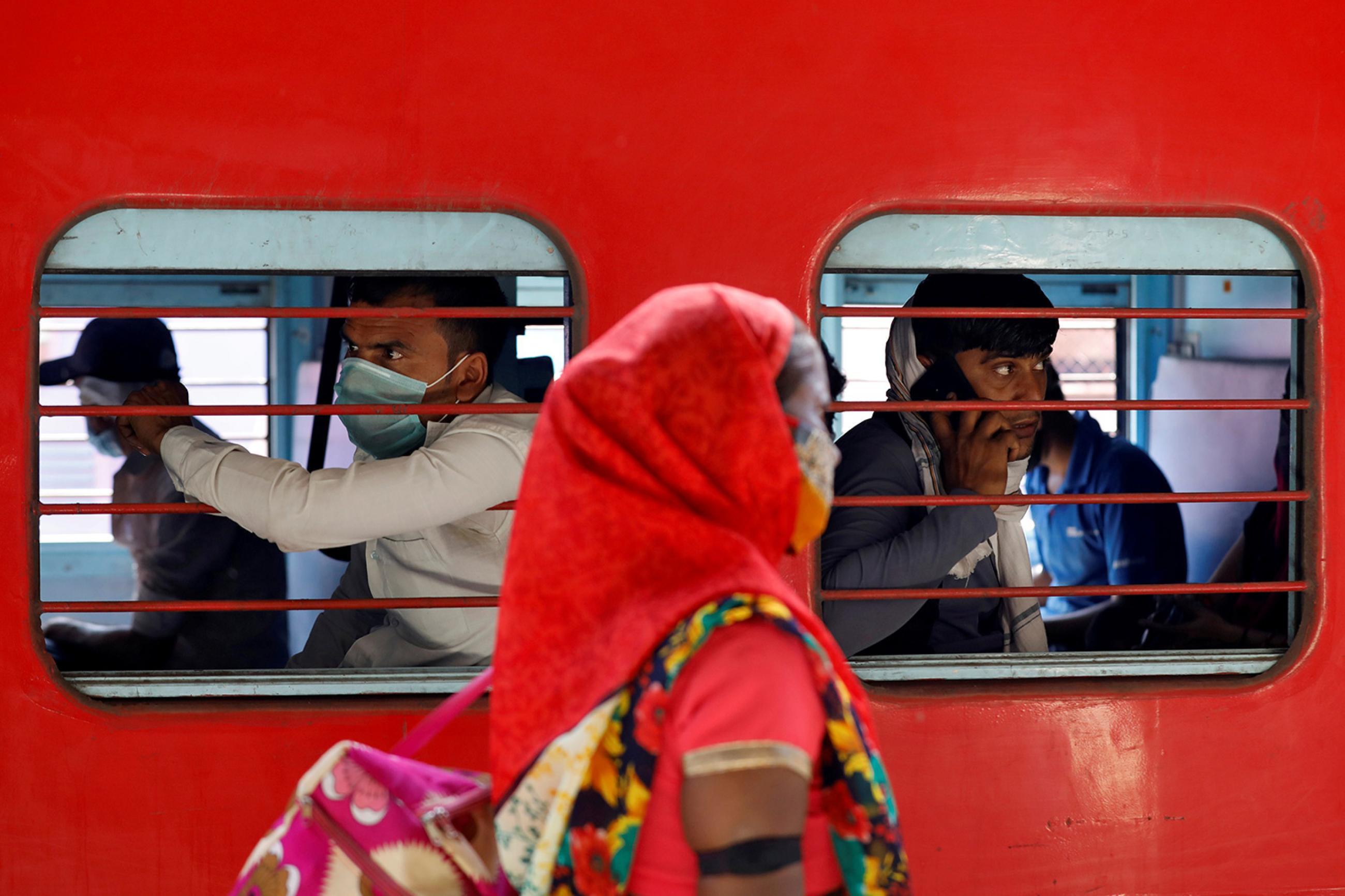 Migrant workers, who were stranded in the western state of Gujarat due to a government lockdown, inside a train as they leave for their homes in Ahmedabad, India, on May 2, 2020. The image shows a bright red train with people inside and a woman walking by the train outside. REUTERS/Amit Dave 