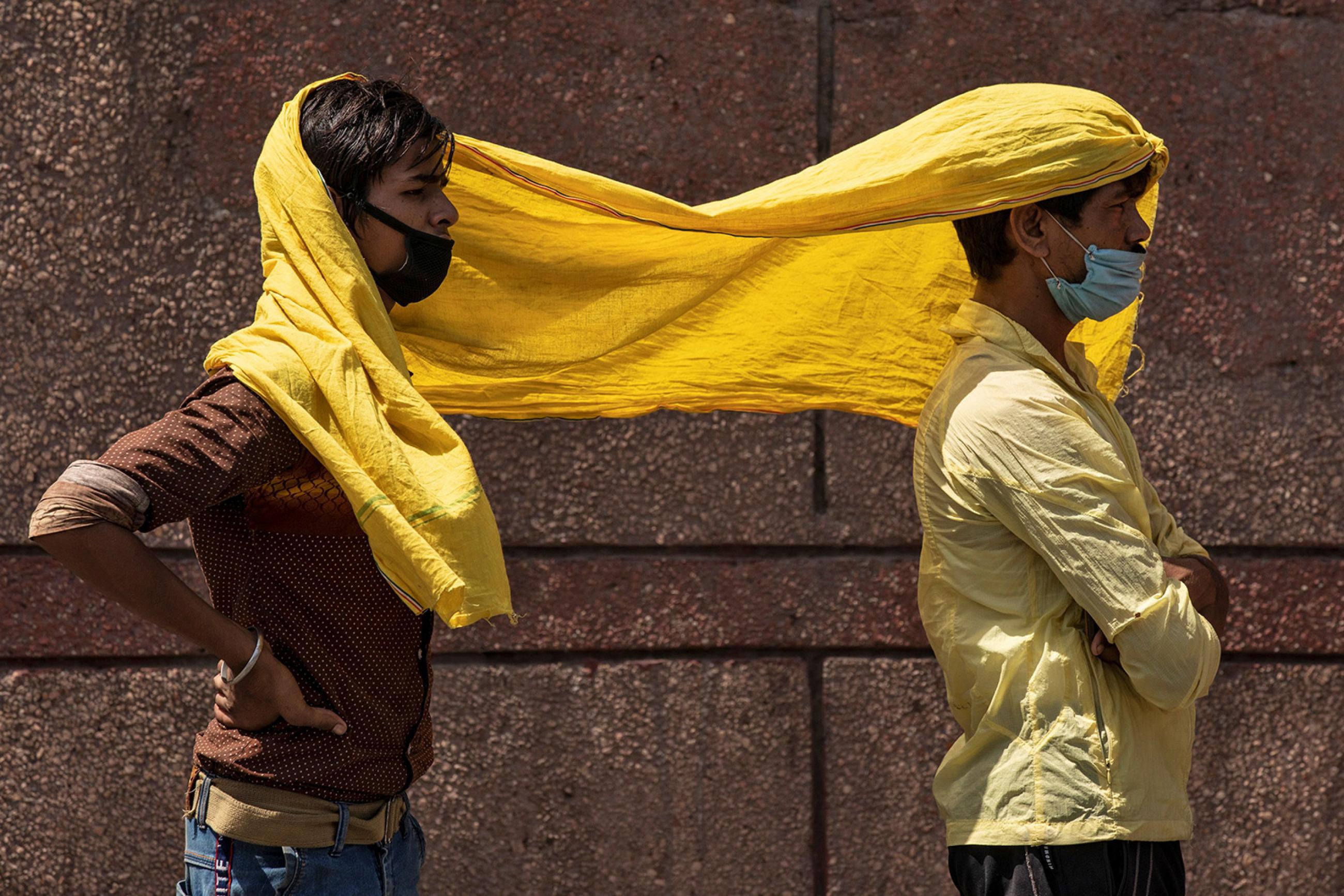 Migrant workers protect themselves from heat as they wait to board a train to their home state of eastern Bihar, at the end of the coronavirus lockdown in New Delhi, India, on May 21, 2020. The image shows two men sharing a yellow scarf. REUTERS/Danish Siddiqui