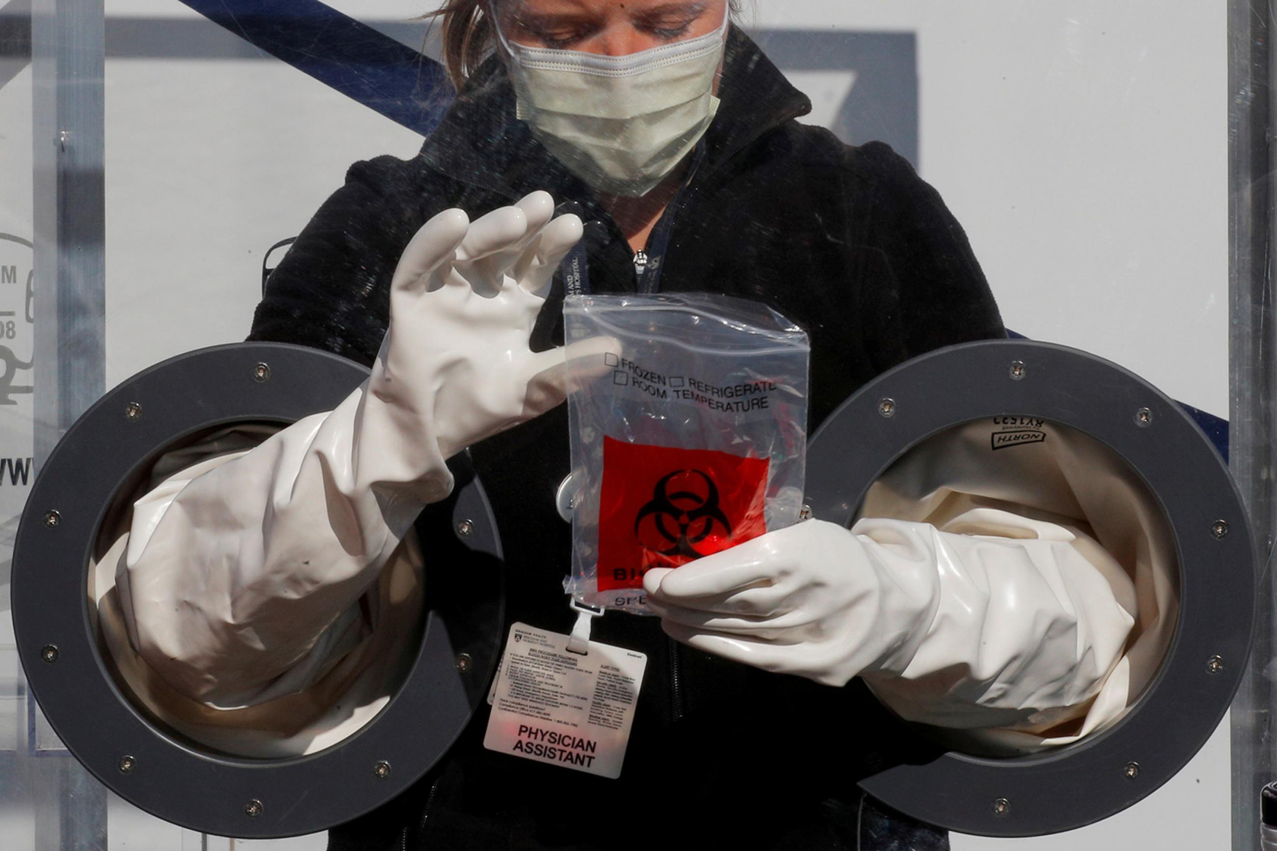 Physician Assistant Cori Kostick demonstrates a booth used to administer tests for coronavirus at the Brigham and Women Hospital in Boston, Massachusetts, on May 5, 2020. The photo shows the worker behind a protective barrier with incorporated gloves, allowing her to work with patients on the other side. REUTERS/Brian Snyder
