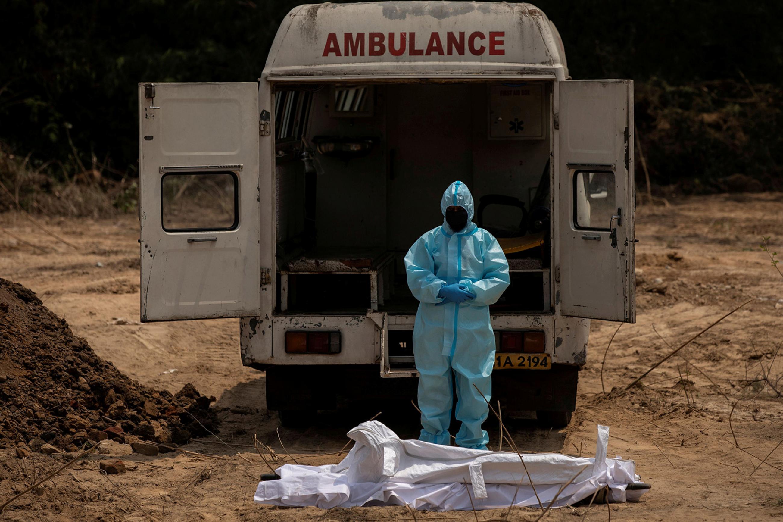 A man offers funeral prayers for a Central Reserve Police Force (CRPF) officer who died from the coronavirus disease (COVID-19), at a graveyard in New Delhi, India, April 29, 2020. The photo shows a man dressed entirely in protective gear with his head bowed in font of an ambulance and before what appears to be a corpse wrapped in white sheets. REUTERS/Danish Siddiqui 