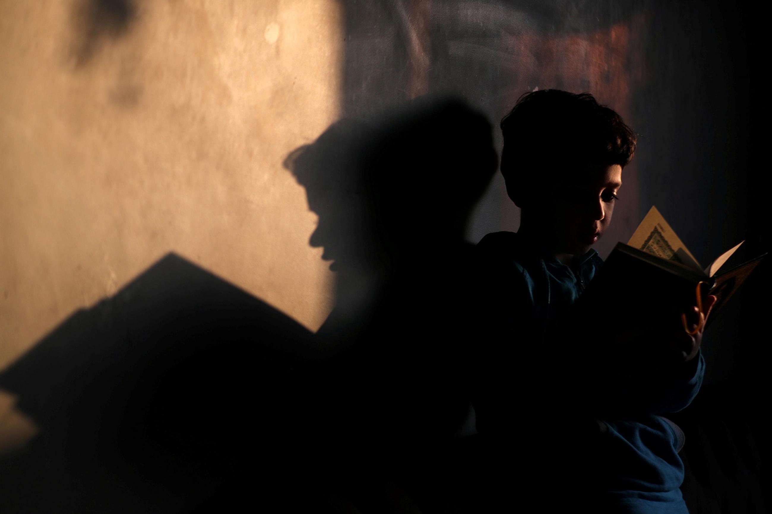 A boy reads the Koran after morning prayers with his family during the holy month of Ramadan, as Egypt ramps up efforts to slow the spread of the coronavirus in Cairo, Egypt, on April 26, 2020. Picture shows the boy reading with his shadow cast on the wall behind him. REUTERS/Mohamed Abd El Ghany