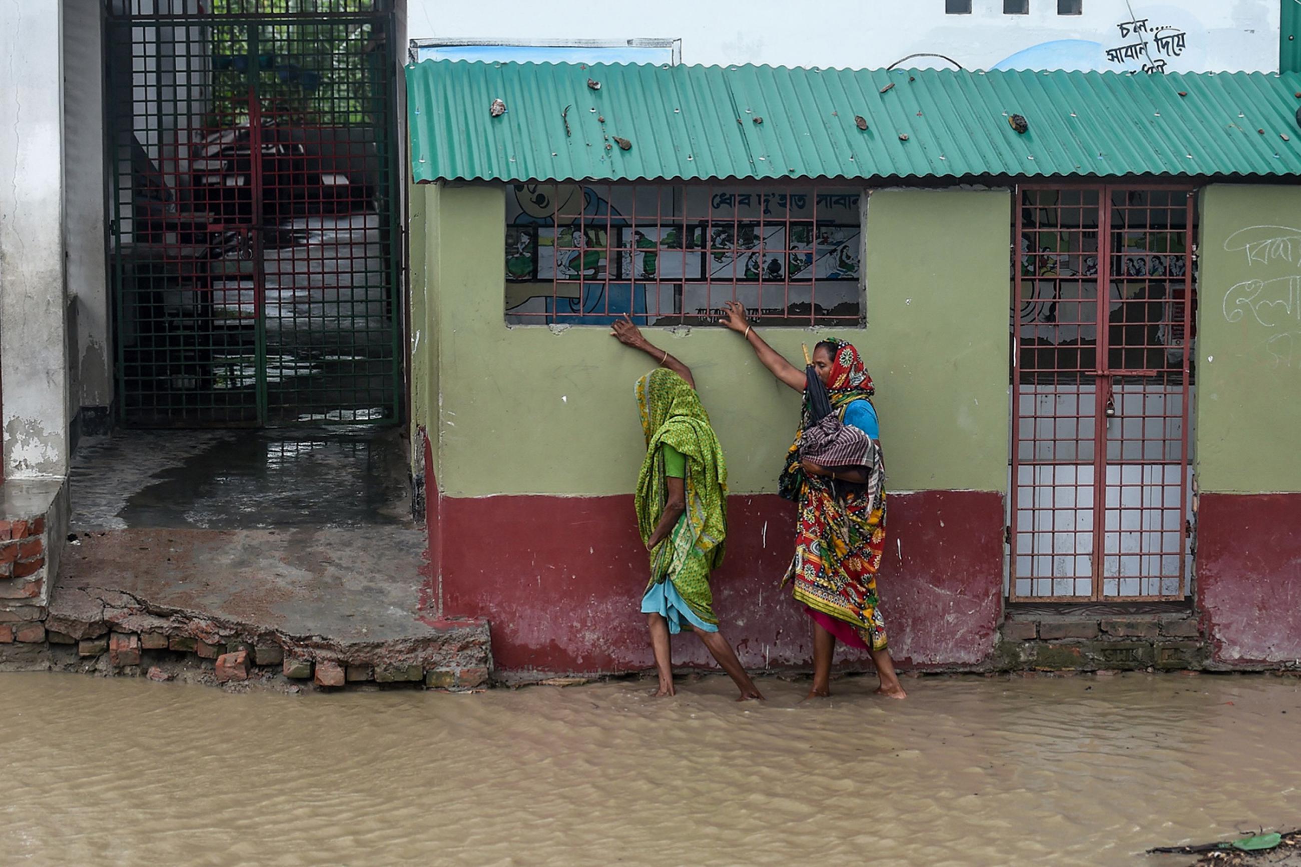 Residents walk along a house on a flooded street heading to a shelter ahead of the expected landfall of the "super cyclone" Amphan, in the Dacope of Khulna district, Bangladesh, on May 20, 2020. Photo shows two people walking and hanging on to a building as they navigate the flooded streets. AFP/Munir uz Zaman via Getty Images