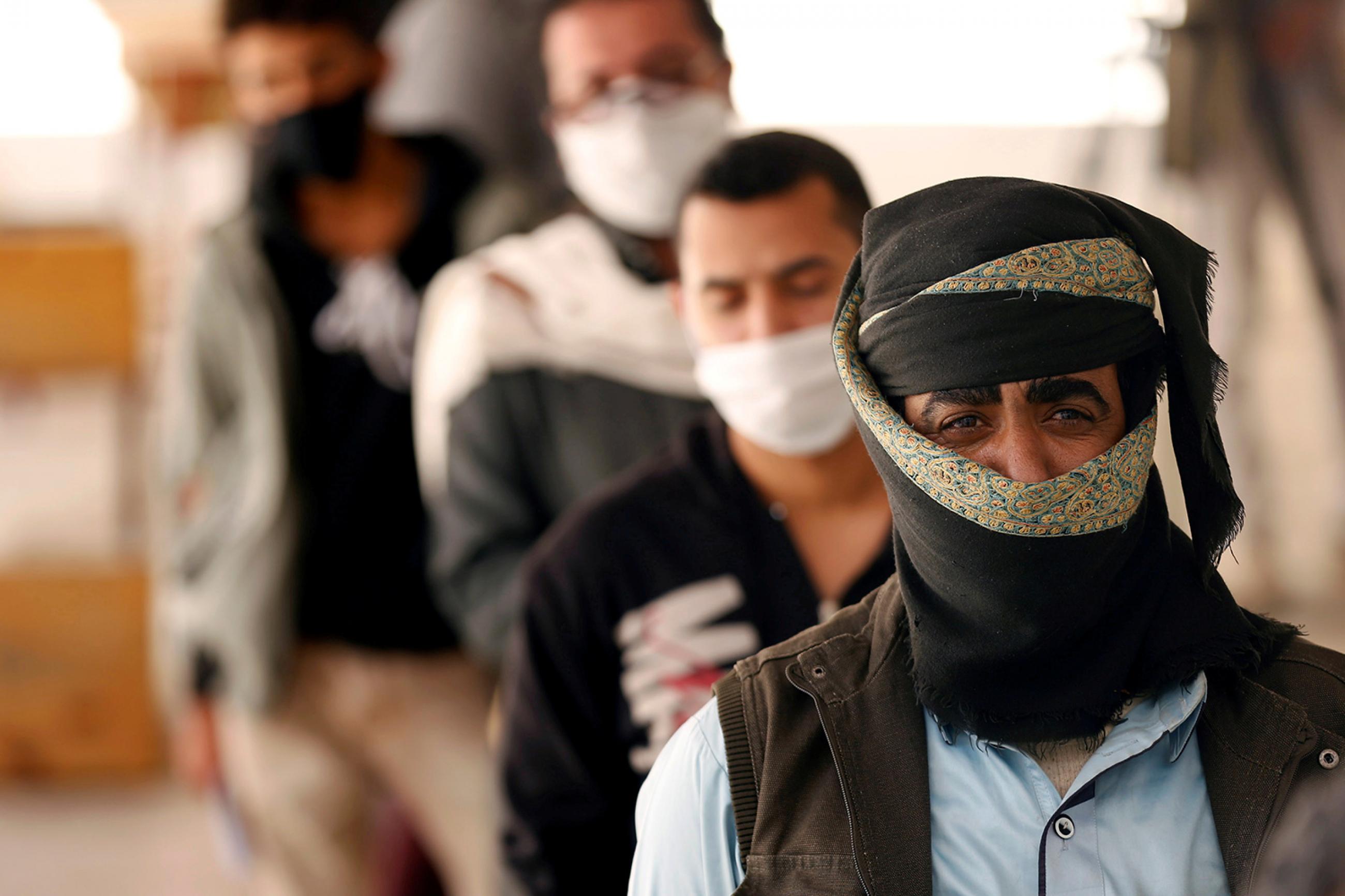 People stand in line to receive vouchers at a food distribution center supported by the World Food Program in Sanaa, Yemen, on June 3, 2020 amid the coronavirus pandemic. The photo shows several men lined up in a queue. They are all wearing facemasks. REUTERS/Khaled Abdullah