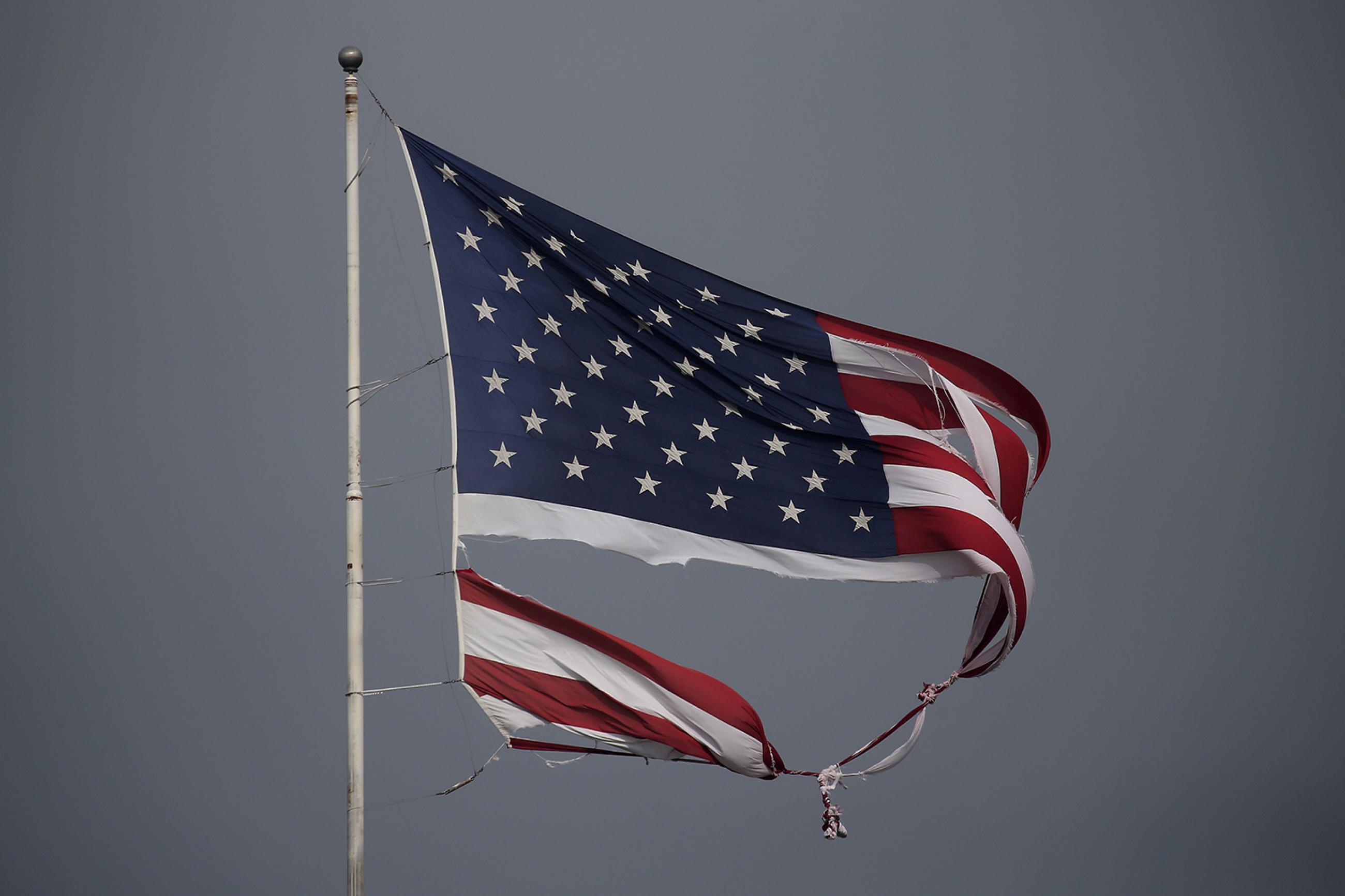 A tattered U.S. flag damaged in Hurricane Harvey, flies in Conroe, Texas, on August 29, 2017. The photo shows a torn U.S. flag blowing against a dark grey sky. REUTERS/Carlo Allegri