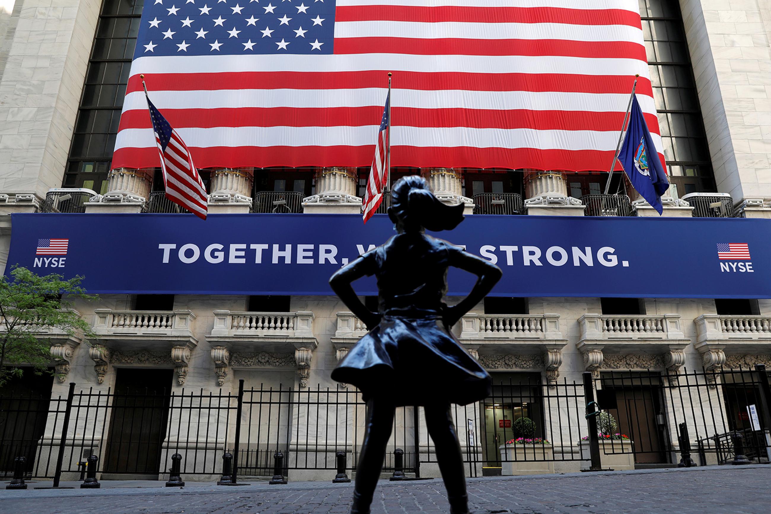 The "Fearless Girl" statue is seen outside the New York Stock Exchange following first trading session since its March coronavirus lockdown in the Manhattan borough of New York City on May 26, 2020. The photo shows the statue with a huge American flag in the background. REUTERS/Mike Segar