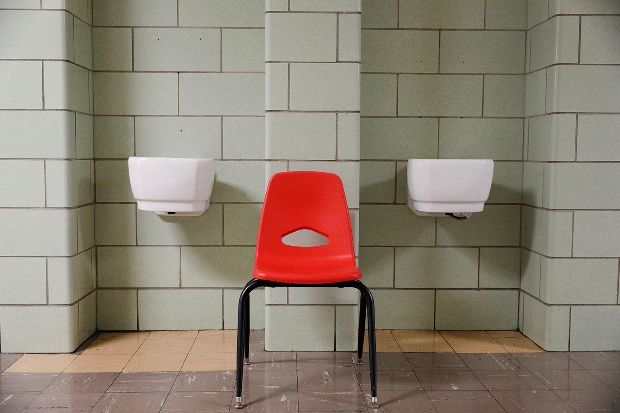 U.S. school systems are stuck between two bad choices. A classroom chair rests between two dismantled water fountains at Edmondson Westside High School in Baltimore, Maryland, on April 28, 2020. The photo shows a red chair in a beige-colorored hallway where two porticos feature white porcelain basins now dry for the pandemic. REUTERS/Tom Brenner