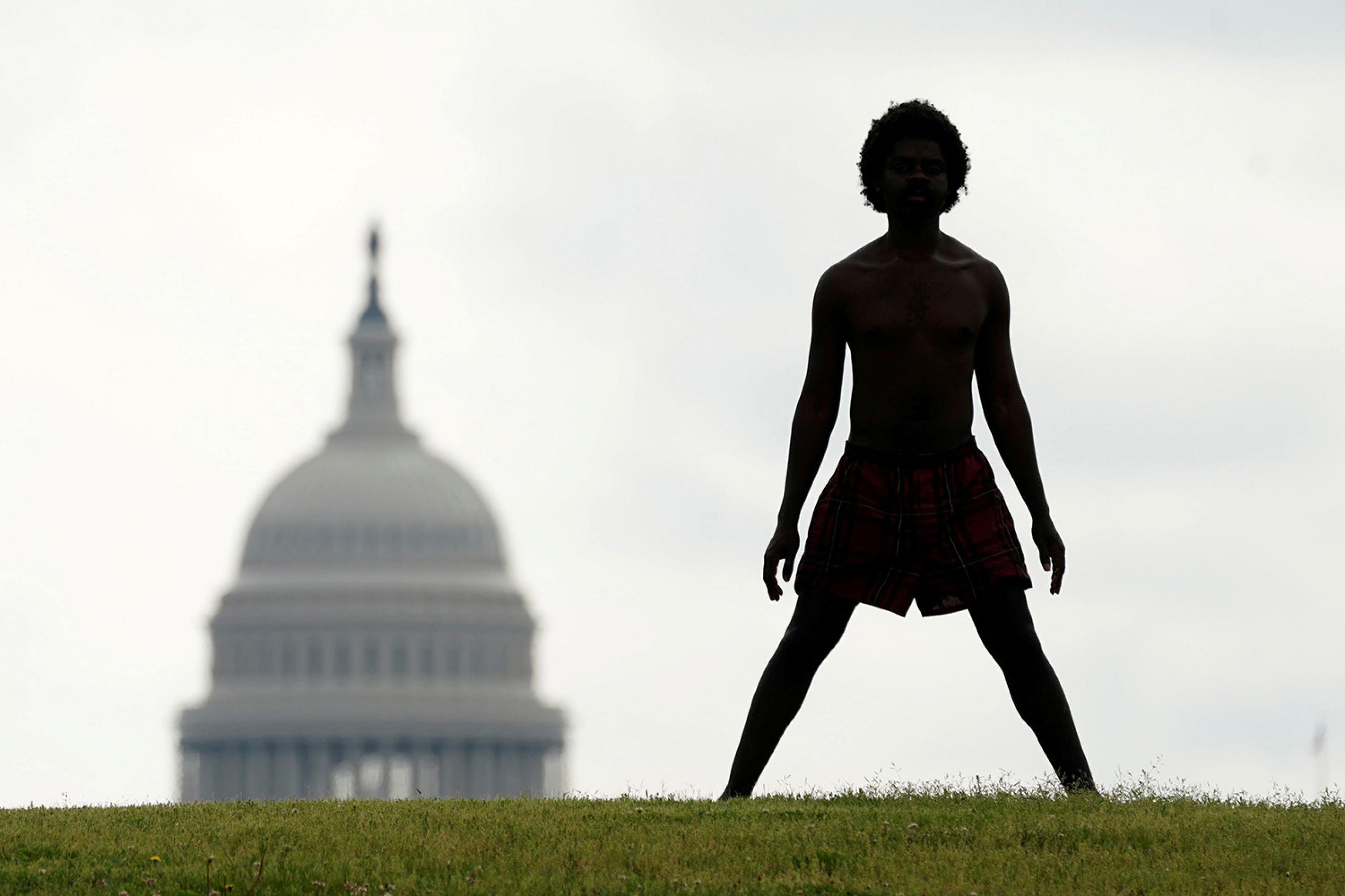 With the dome of the U.S. Capitol in the background, a homeless man named Damu stretches on the National Mall in Washington, U.S., May 27, 2020. The photo is striking, with a man in silhouette standing on a hill with his legs spread wide. in the background slightly to his left is the congressional building. REUTERS/Kevin Lamarque 