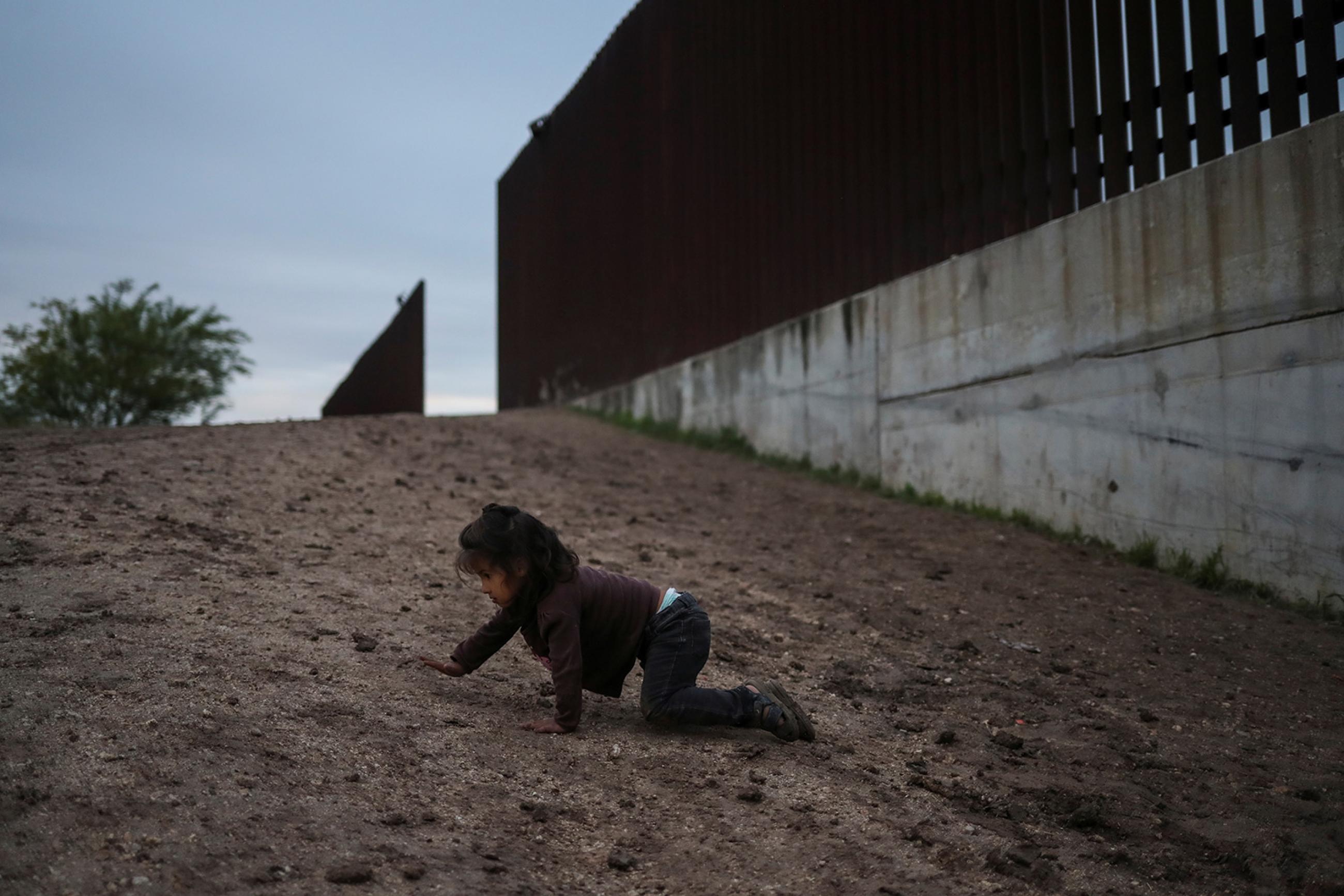 Amy, a two-year-old migrant from Honduras seeking asylum with her parents, crawls on a dirt road after crossing the Rio Grande river into the United States in Penitas, Texas, on April 1, 2019. The photo shows a small child craling on the ground near a giant border fence. REUTERS/Adrees Latif