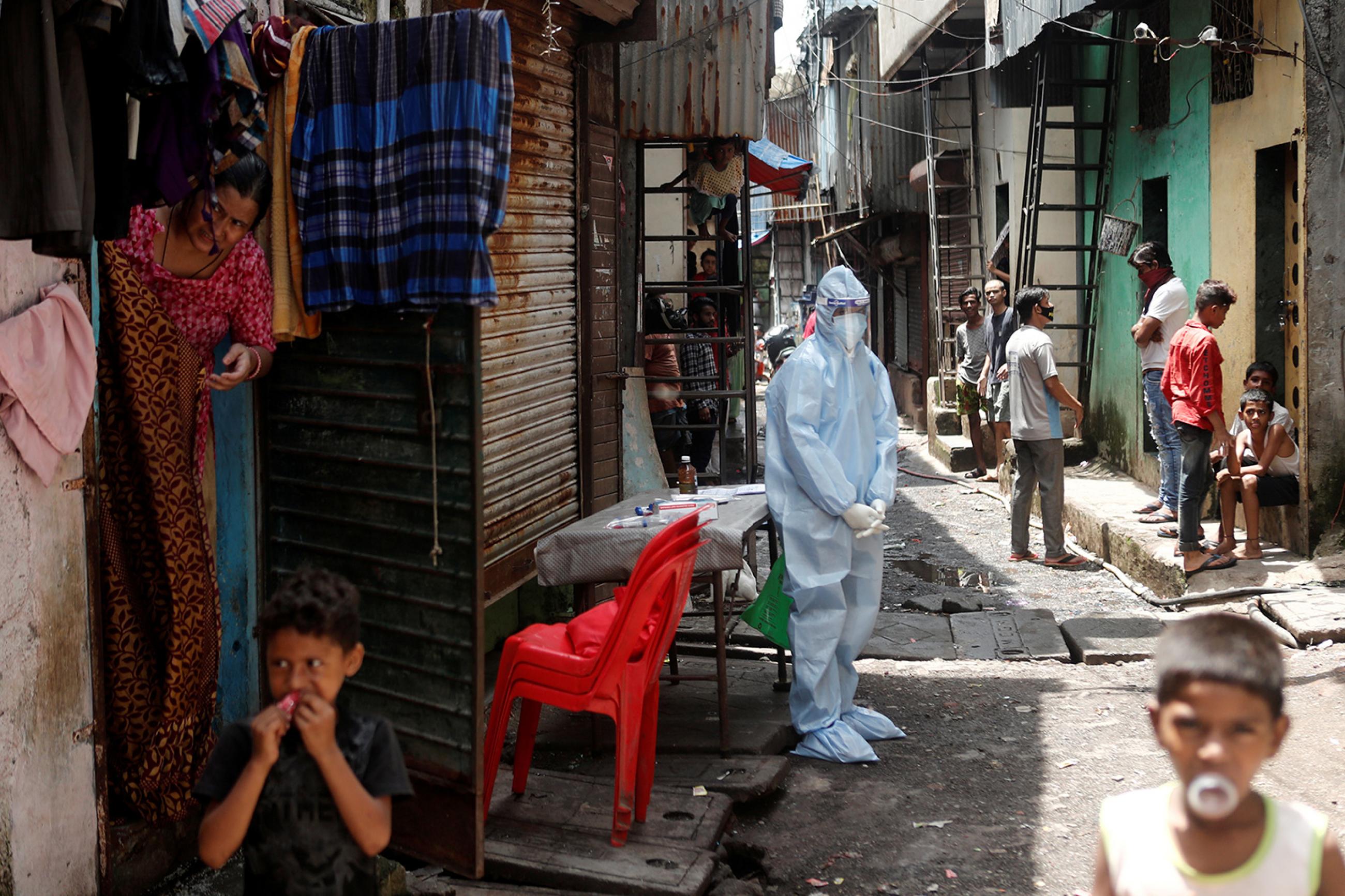 A health-care worker waits to test residents during a medical campaign for the coronavirus disease (COVID-19) at a slum area in Mumbai, India, June 30, 2020. The photo shows a worker wearing personal protective equipment standing awkwardly among residents, most of whom aren't even wearing a mask. REUTERS/Francis Mascarenhas