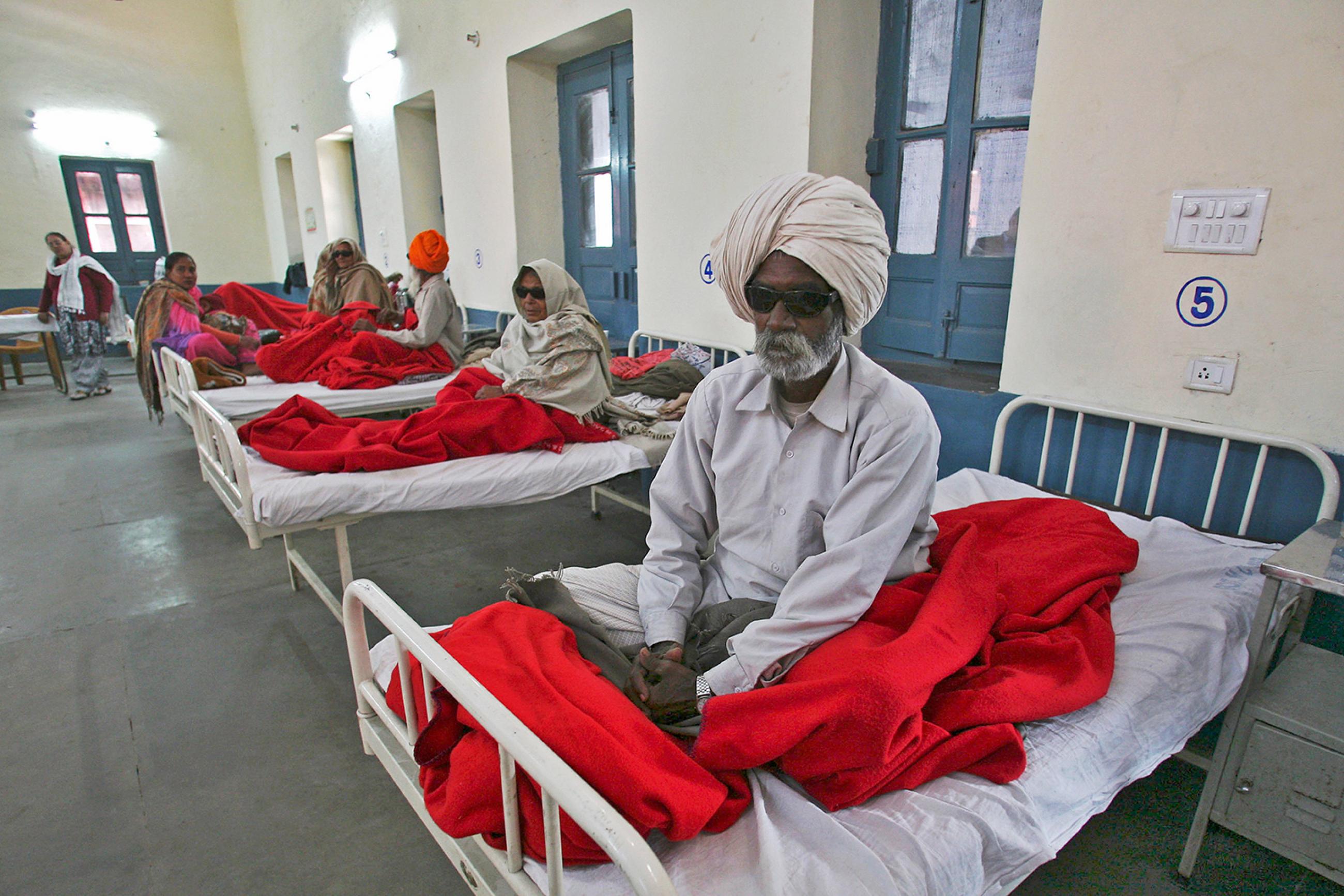 People waiting for treatment at a hospital after undergoing cataract removals from a free but shoddy eye surgery camp that caused them to lose their vision—in Amritsar, India, on December 5, 2014. The photo shows several people sitting on hospital beds. One man in the foreground is wearing dark glasses. REUTERS/Munish Sharma