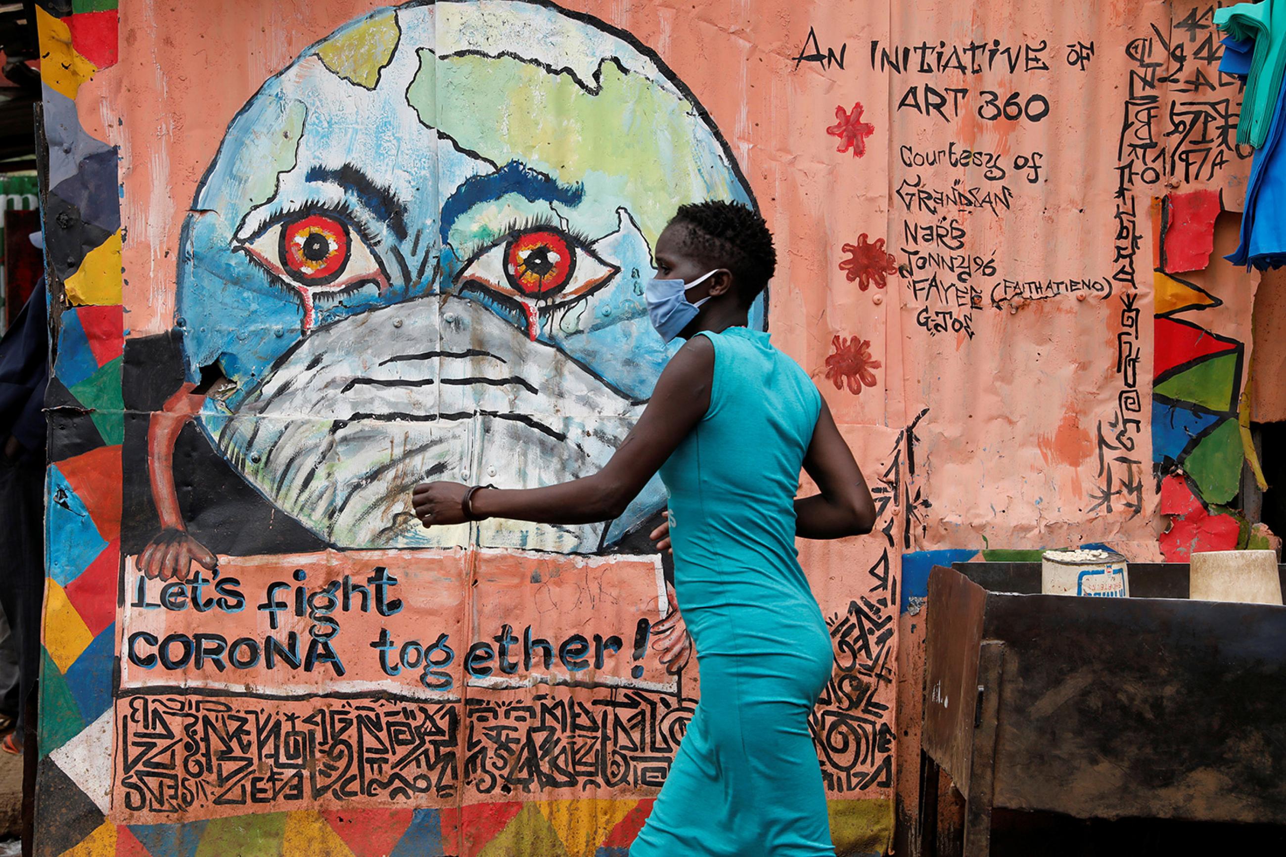 A woman walks past a graffiti promoting the fight against the spread of the coronavirus disease (COVID-19) in the Kibera slums of Nairobi, Kenya, on May 22, 2020. This is a striking photo of a woman in a blue dress wearing a facemask walking past a peach-colored wall with a graffiti of the Earth, also wearing a facemask, with bloodshot eyes and crying. REUTERS/Baz Ratner