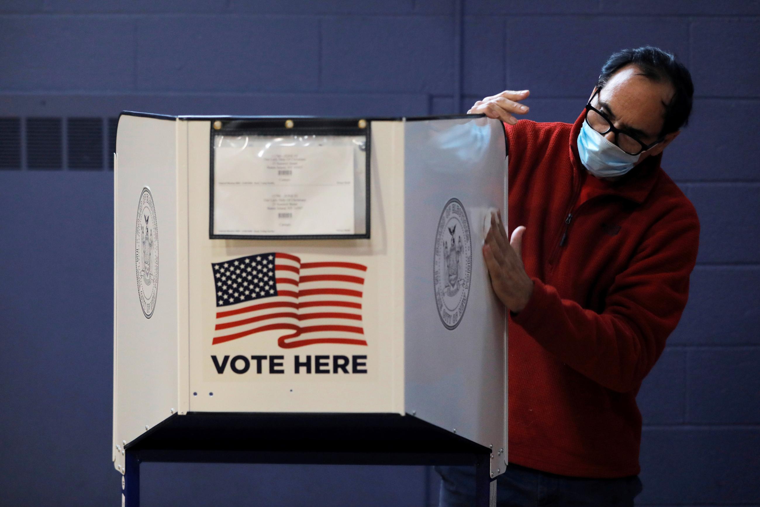 A man sanitizes a privacy booth to fight the spread of COVID-19 at a polling station in New York City, United States, on October 25, 2020. REUTERS/Andrew Kelly