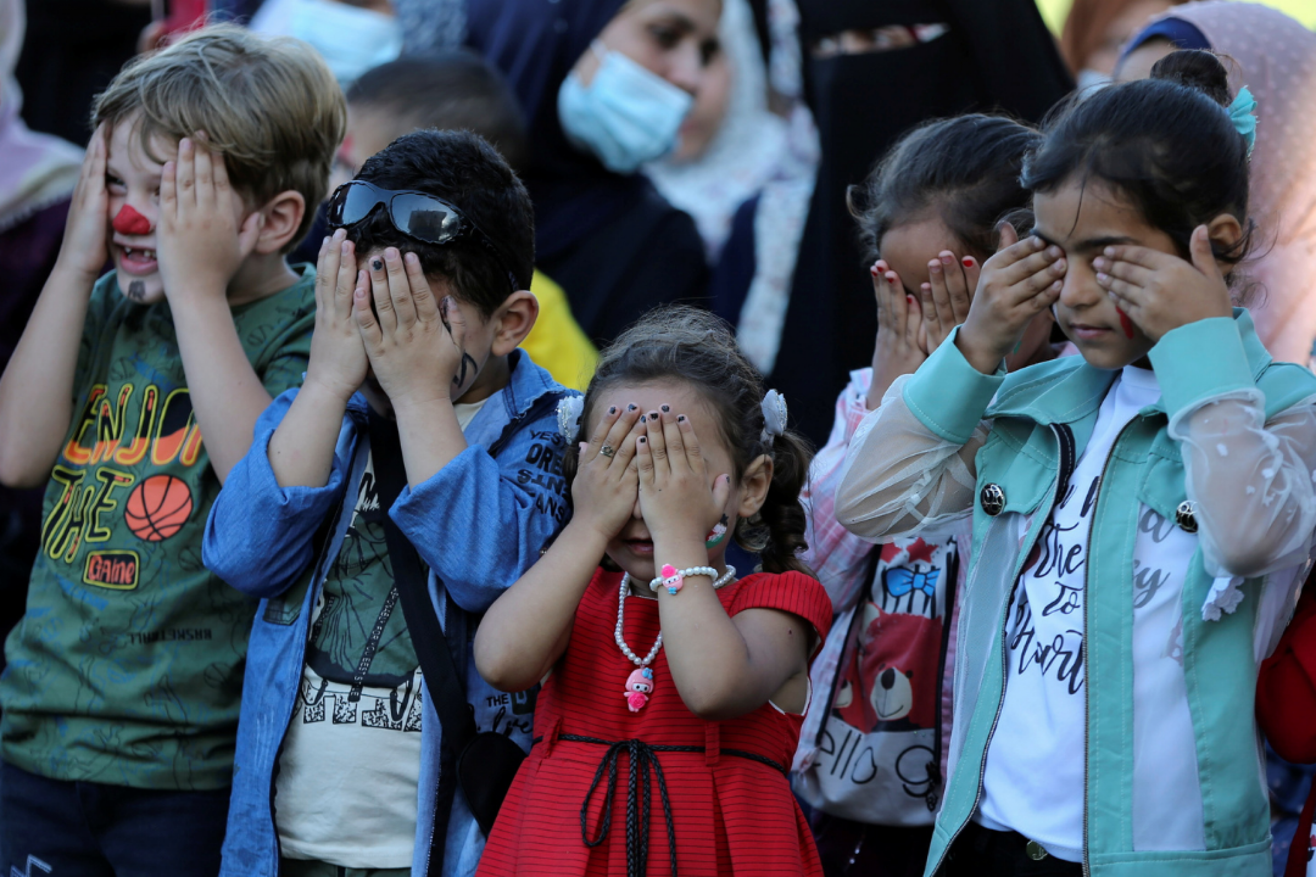 Palestinian children cover their eyes as they participate in a mental health support session in Khan Younis in the southern Gaza Strip on June 6, 2021.