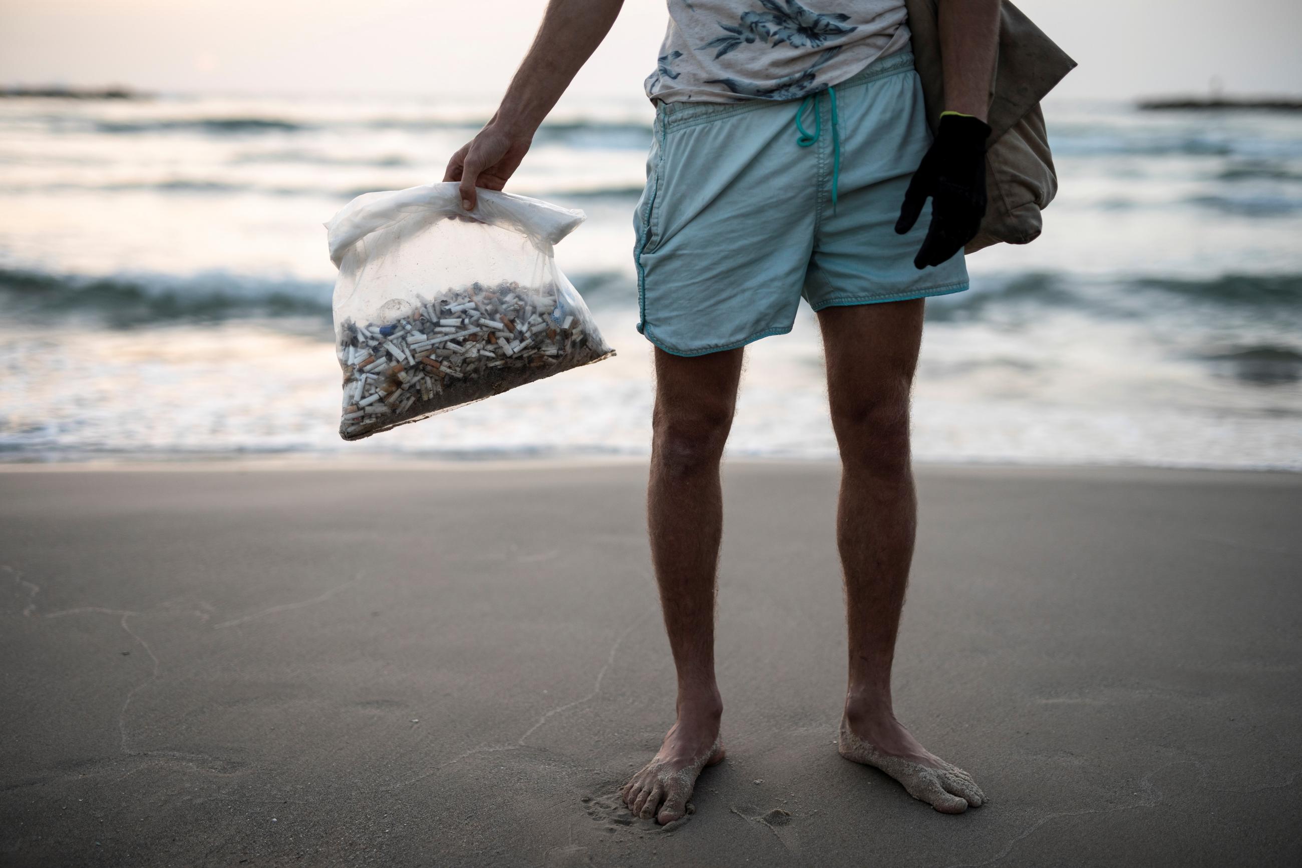 Julian Melcer (only his lower body can be seen) holds a plastic bag filled with cigarette butts he collected from the shore of the Mediterranean Sea at a beach in Tel Aviv, Israel, on April 20, 2021. 