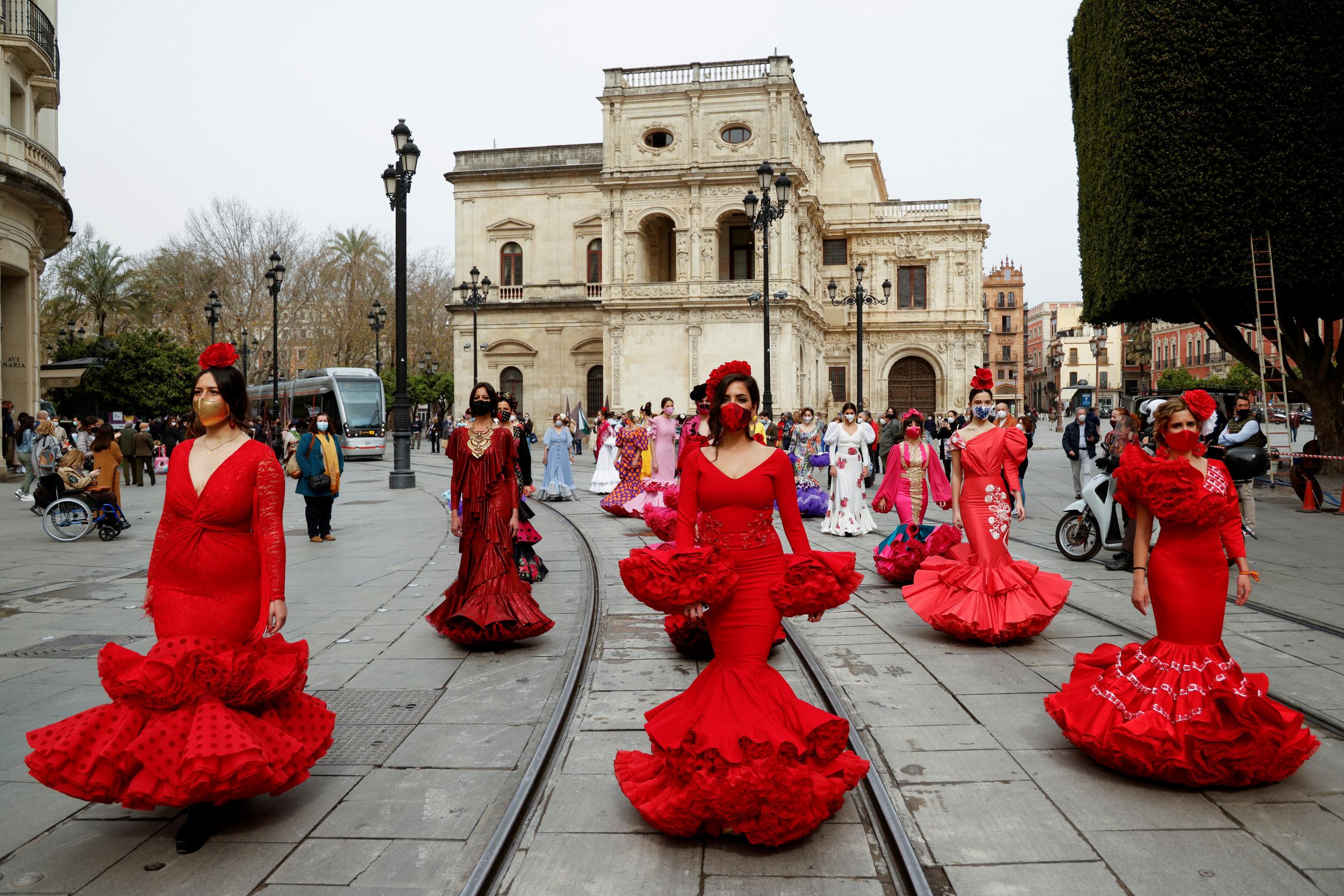 women dressed in traditional flamenco dresses walk in a city square 