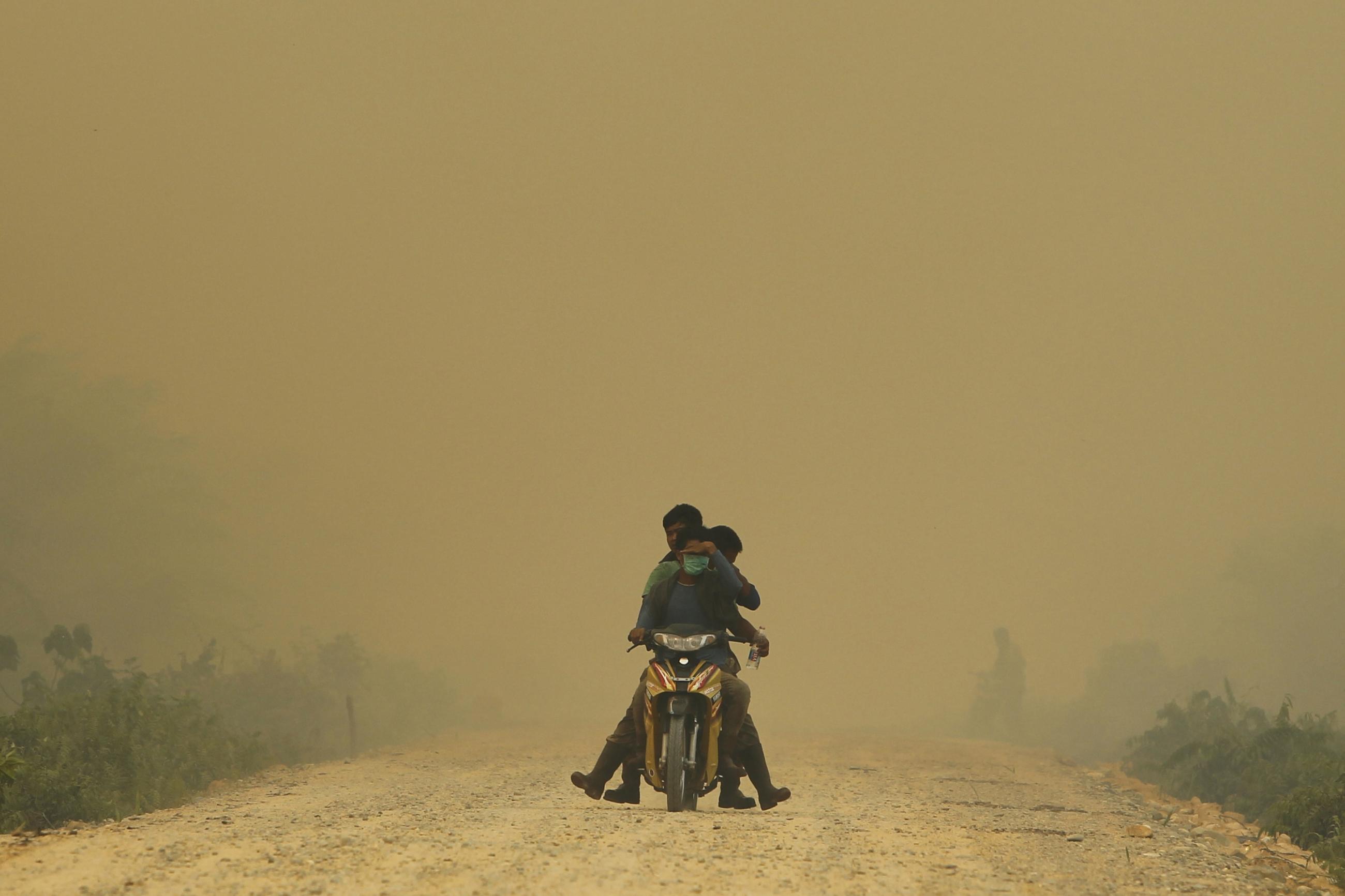 Villagers ride a motorcycle in a haze hit Dumai, in Indonesia's Riau provinc