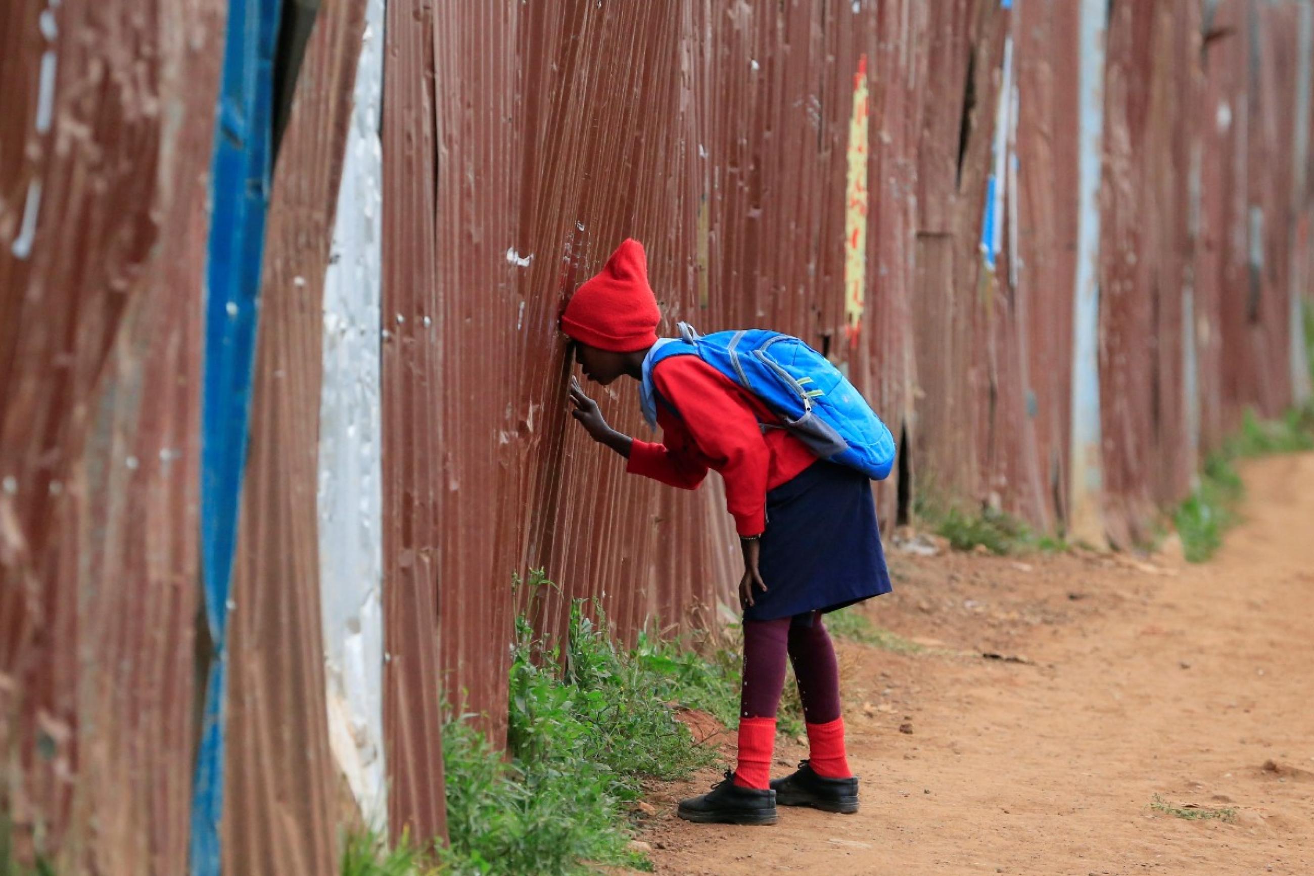 A girl in a red uniform peeks through the fence of her school in Nairobi, Kenya, after the 2021 school year was delayed