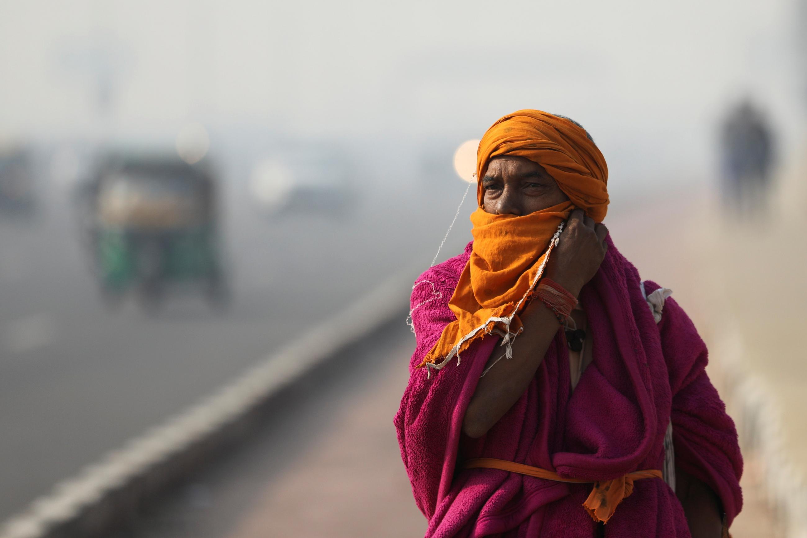 A Sadhu or a Hindu holy man robed in pink and orange adjusts a cloth on his face as he walks across a highway on a smoggy morning in New Delhi, India, November 18, 2021