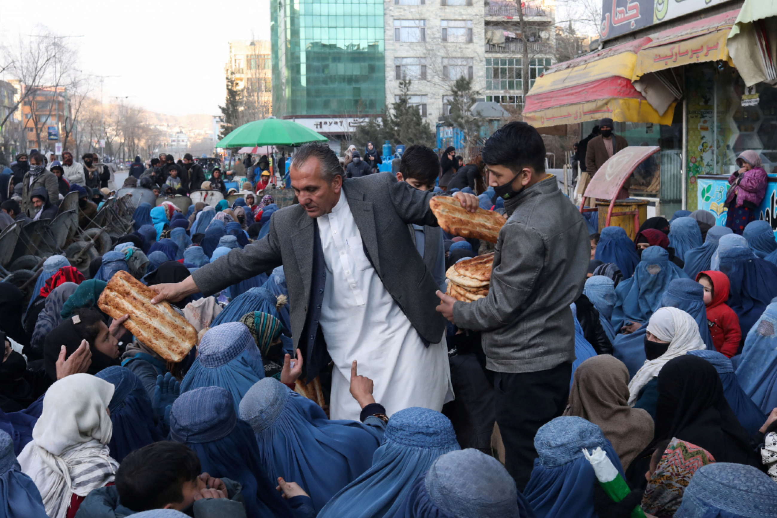 Mehr del Khan Rahmati, who is in charge of a bakery, passes a large flat piece of bread to people awaiting food, in Kabul, Afghanistan, January 31, 2022. 