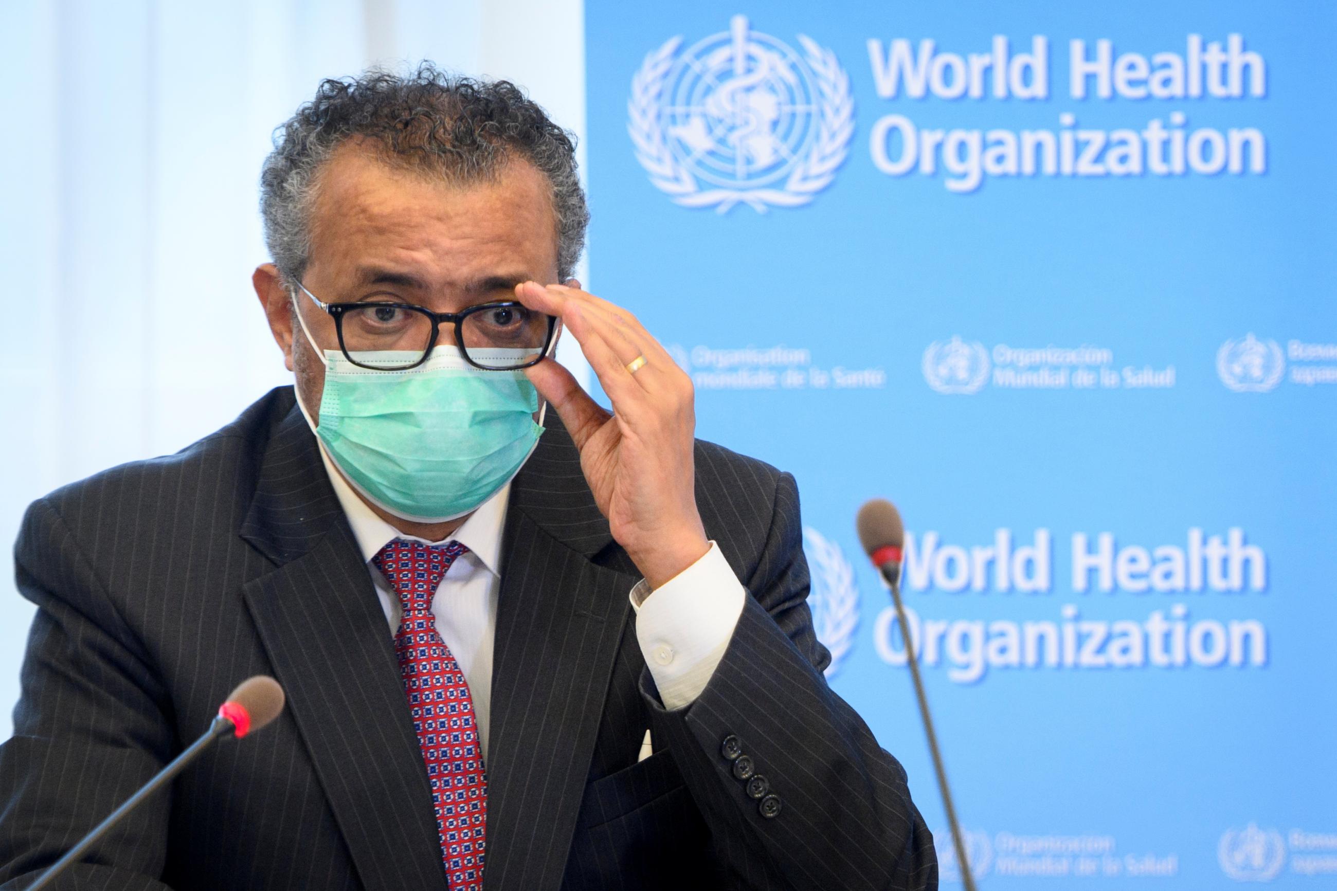 dr. tedros adjusts his glasses while sitting on a WHO panel