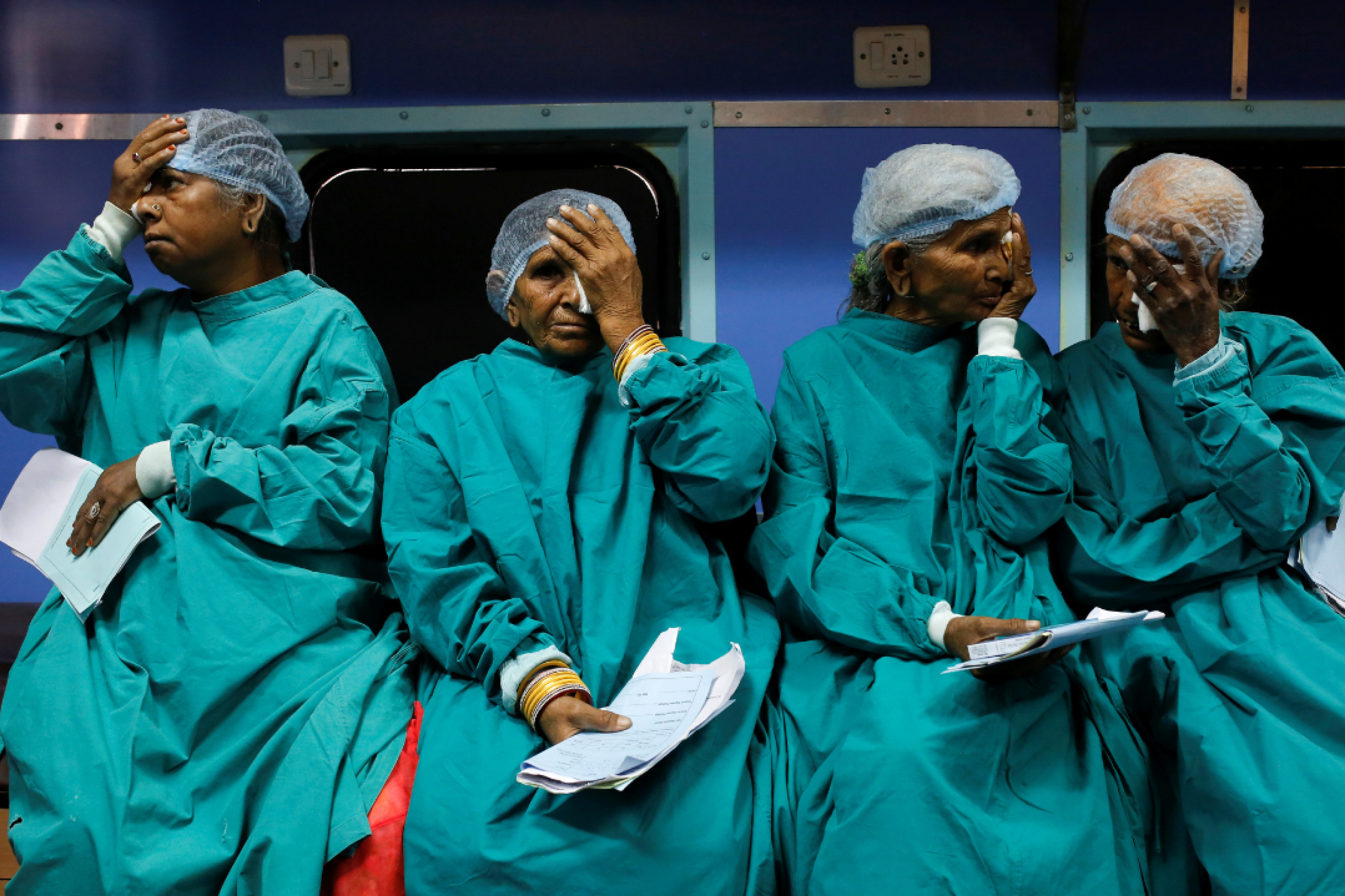 Four older patients dressed in medical gowns cover their eyes as they wait for cataract surgery on the Lifeline Express, a hospital built inside a seven-coach train, at a railway station in Jalore, India, on March 31, 2018. 