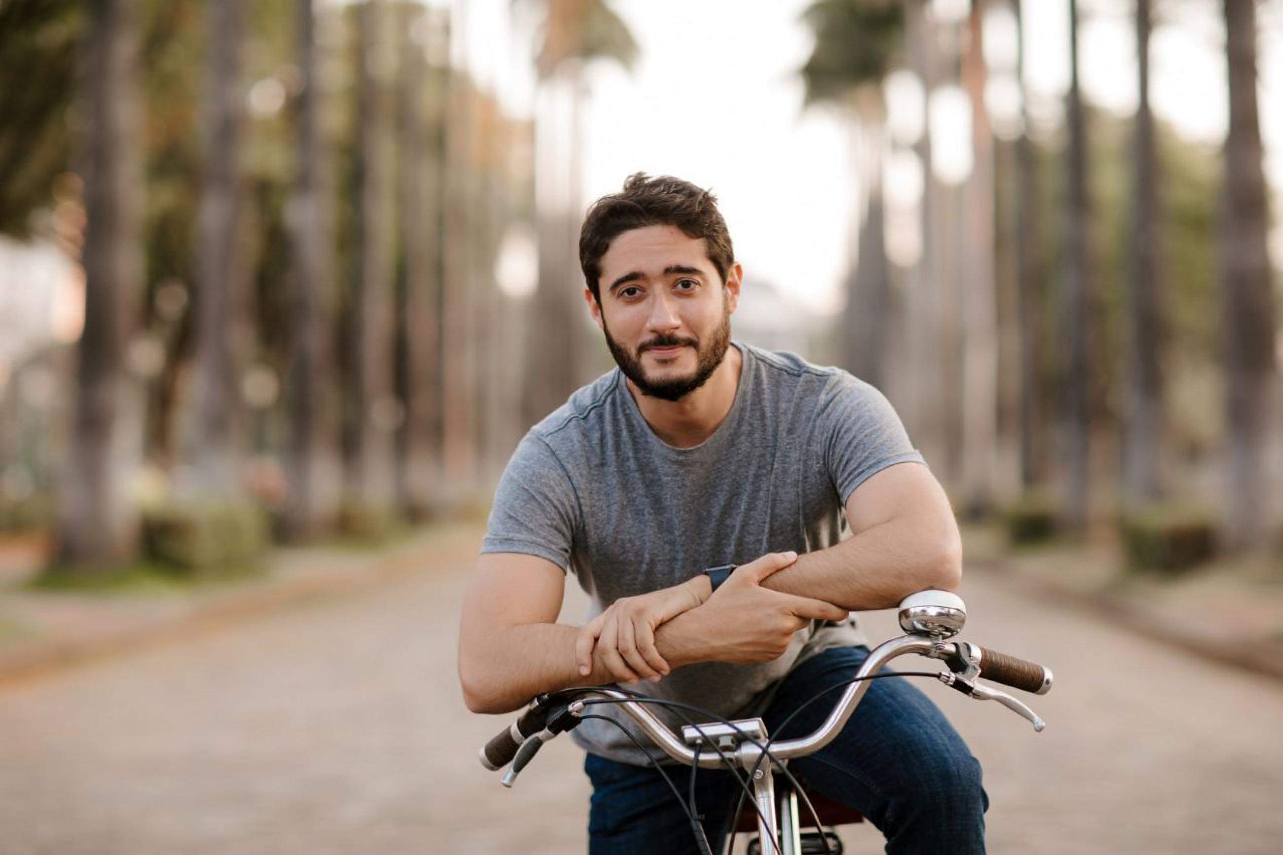 Mayor of Belo Horizonte, Gabriel Azevedo, sporting a grey t-shirt, rides a bike in front of tall trees at Praça da Liberdade, one of the most important touristic sites of Belo Horizonte, Brazil in July 2020.