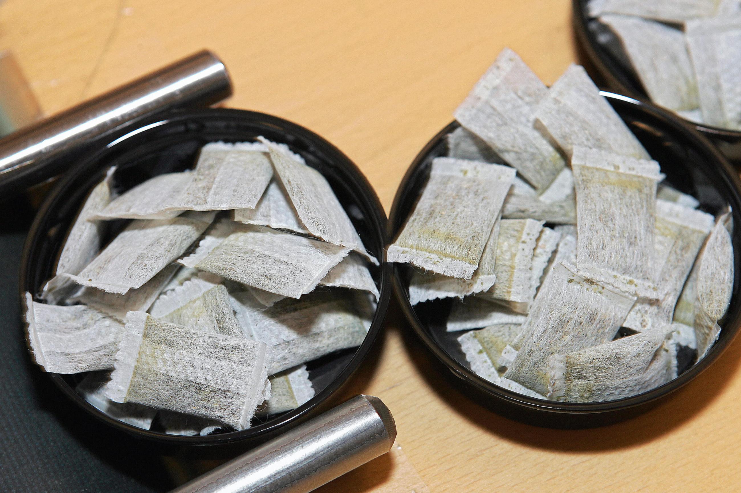 Small pouches containing nicotine are seen scattered across two black tins on a factory production line in Sweden.