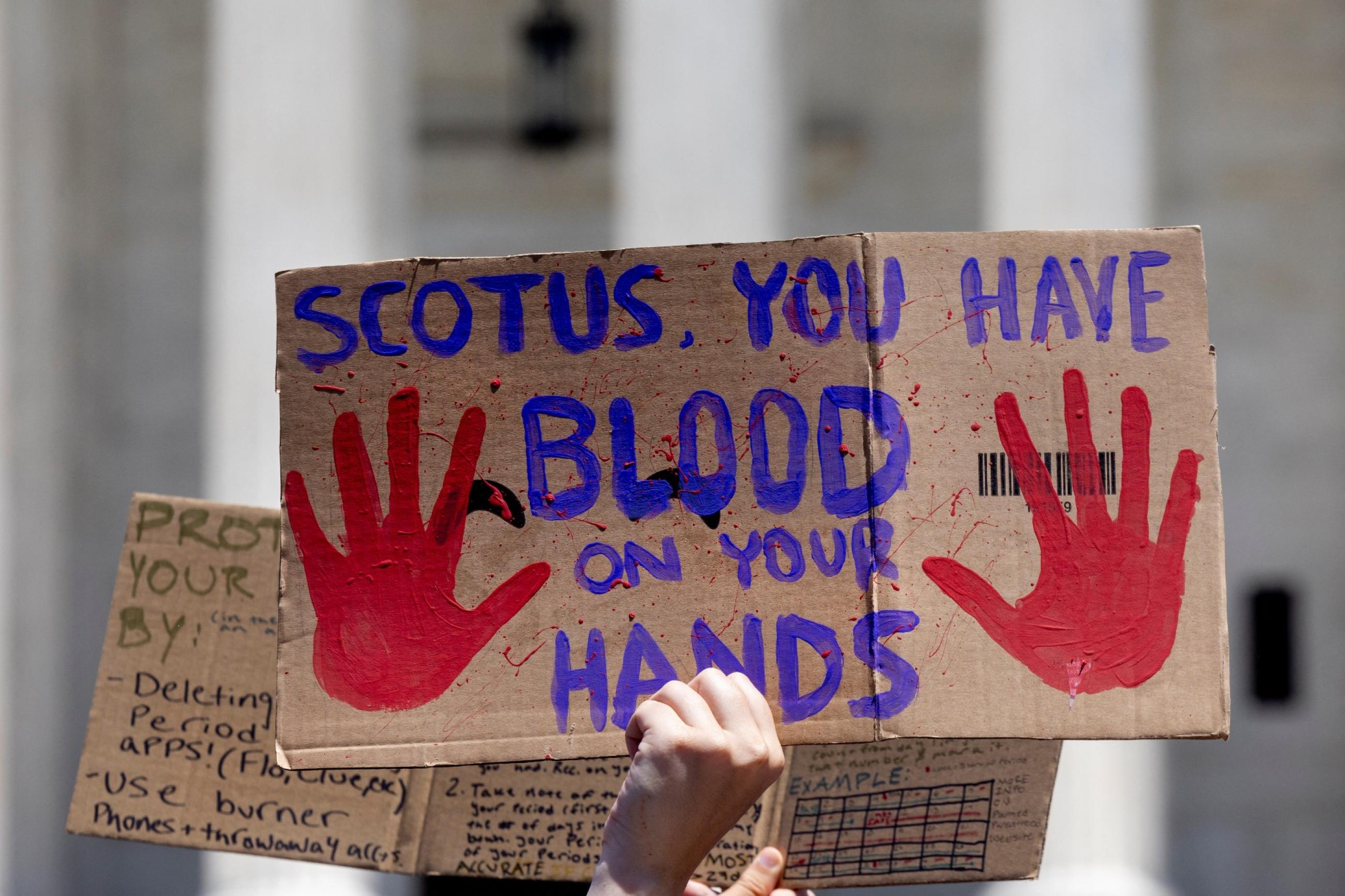 a cardboard signs reads "SCOTUS you have blood on your hands"