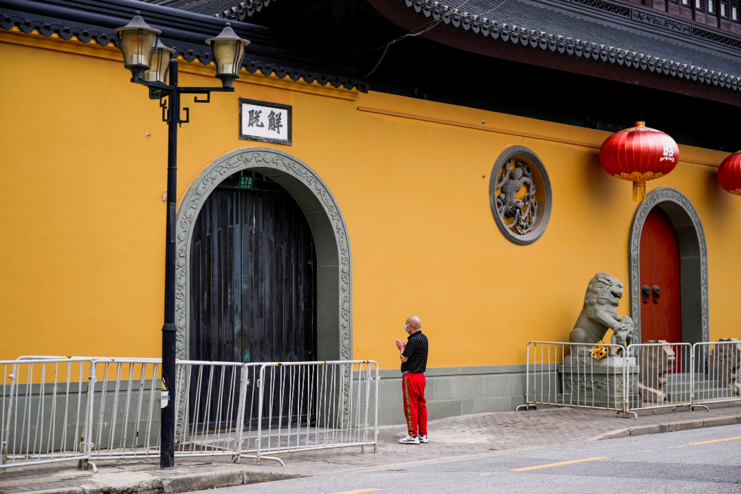 During a lockdown, a man in a mask, red pants, and a black shirt prays outside a bright orange temple that is closed due to a COVID-19 outbreak, in Shanghai, China, on May 30, 2022. in front of a temple