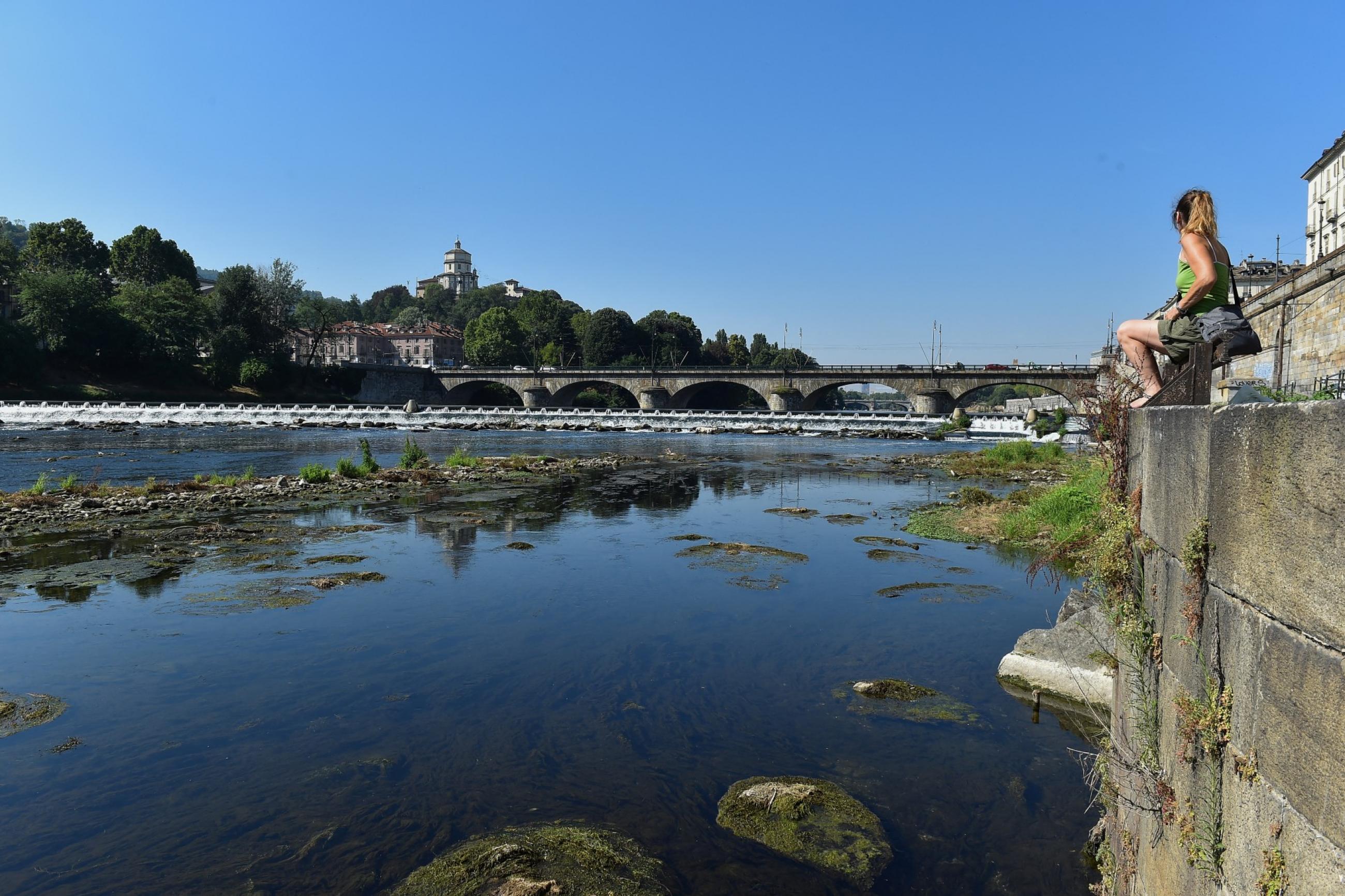 A woman sits next to Po's dry riverbed, as parts of Italy's longest river have dried up due to the worst drought in the last 70 years, in Turin, Italy