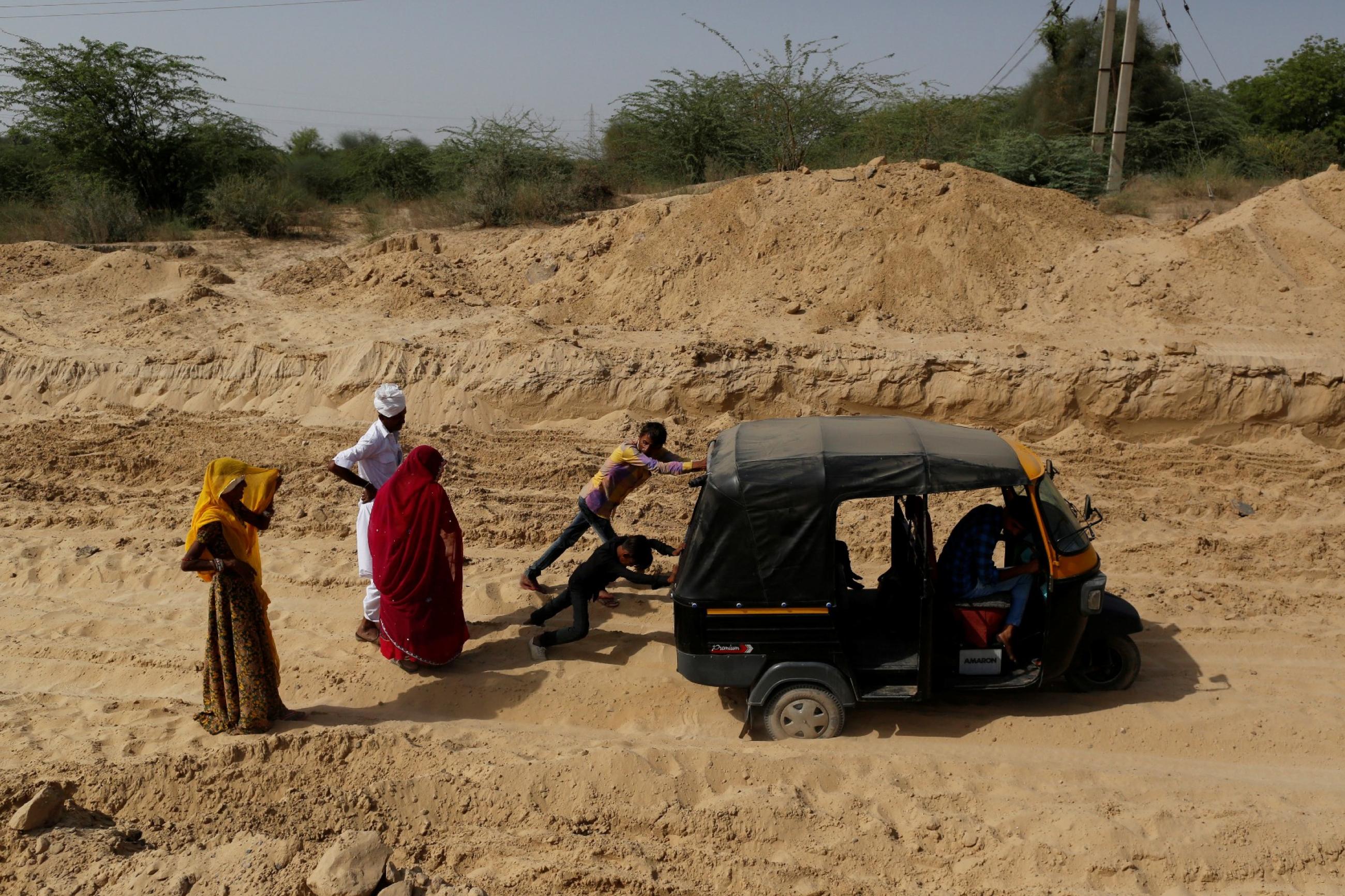 Bhawri Devi watches as her husband and son push an auto-rickshaw which got stuck in the sand on the way home from receiving cancer treatment, in a village in Jalore, India, on April 7, 2018. 