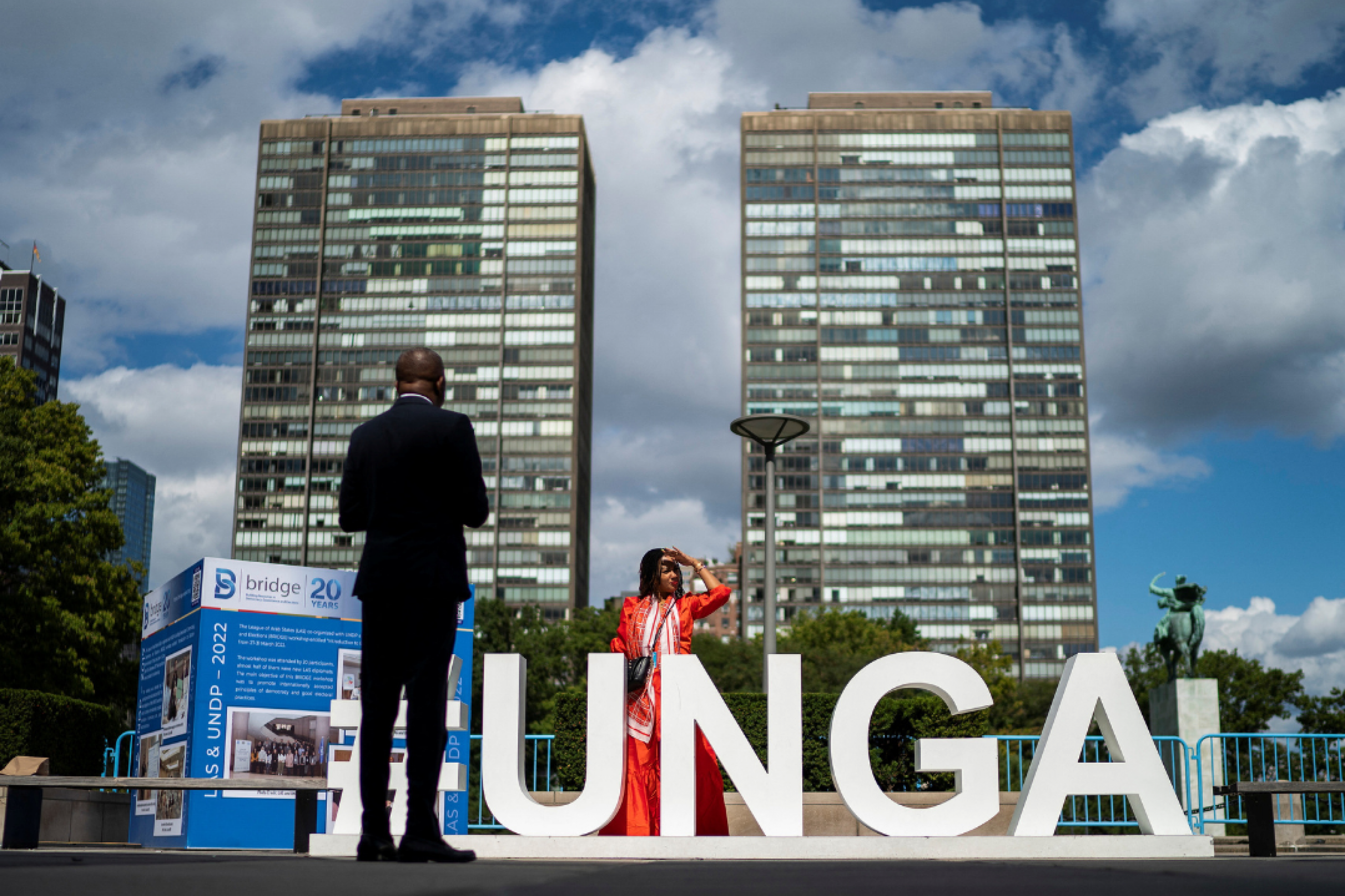 People stand outside the 77th Session of the United Nations General Assembly, where giant white letters UNGA stand on the ground, at UN Headquarters in New York, on September 20, 2022. 