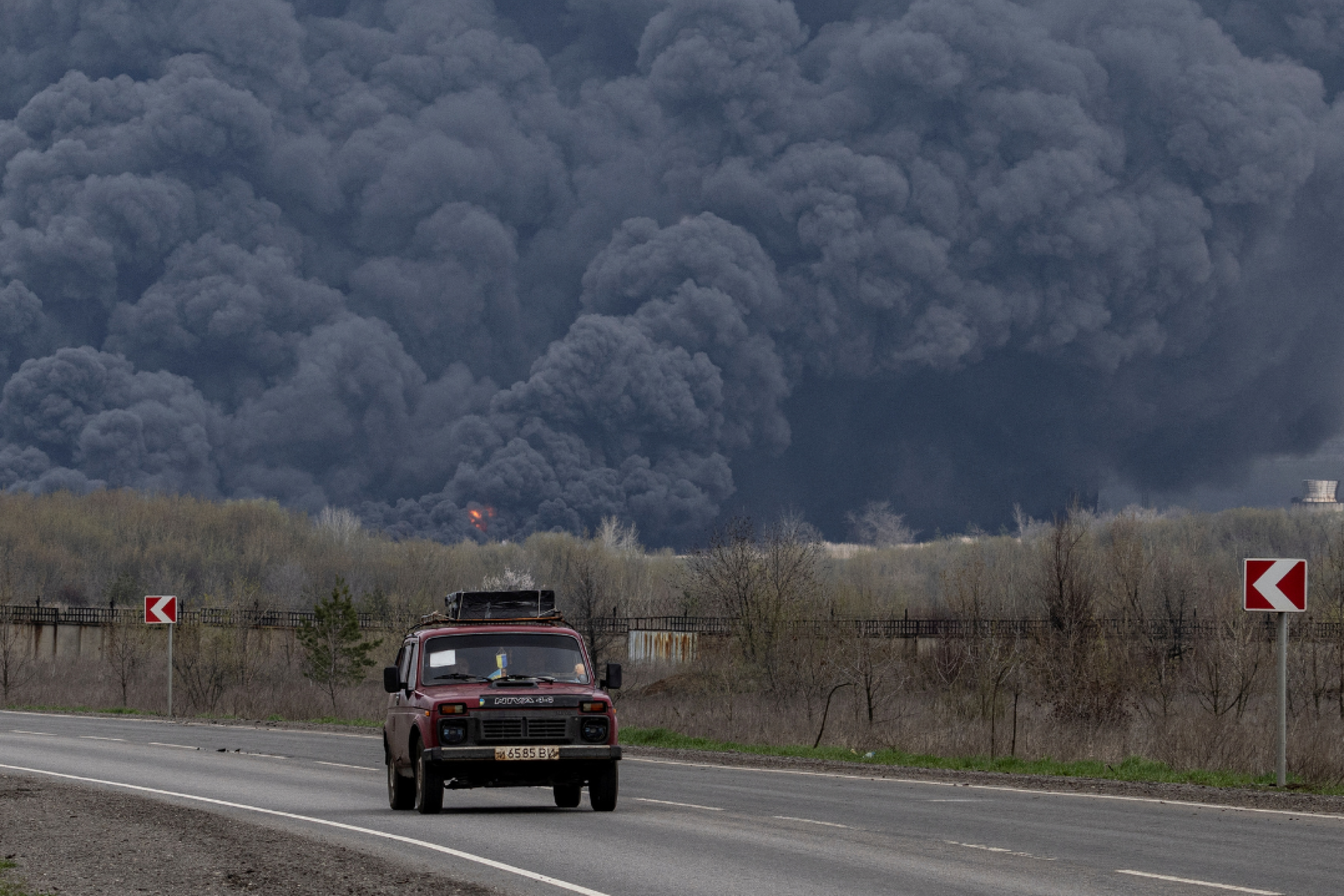 Plumes of black smoke rise up into the air behind a car as it passes the Lysychansk Oil Refinery after if was hit by a missile at Lysychansk, in the Luhansk region, Ukraine, on April 16, 2022. REUTERS/Marko Djurica