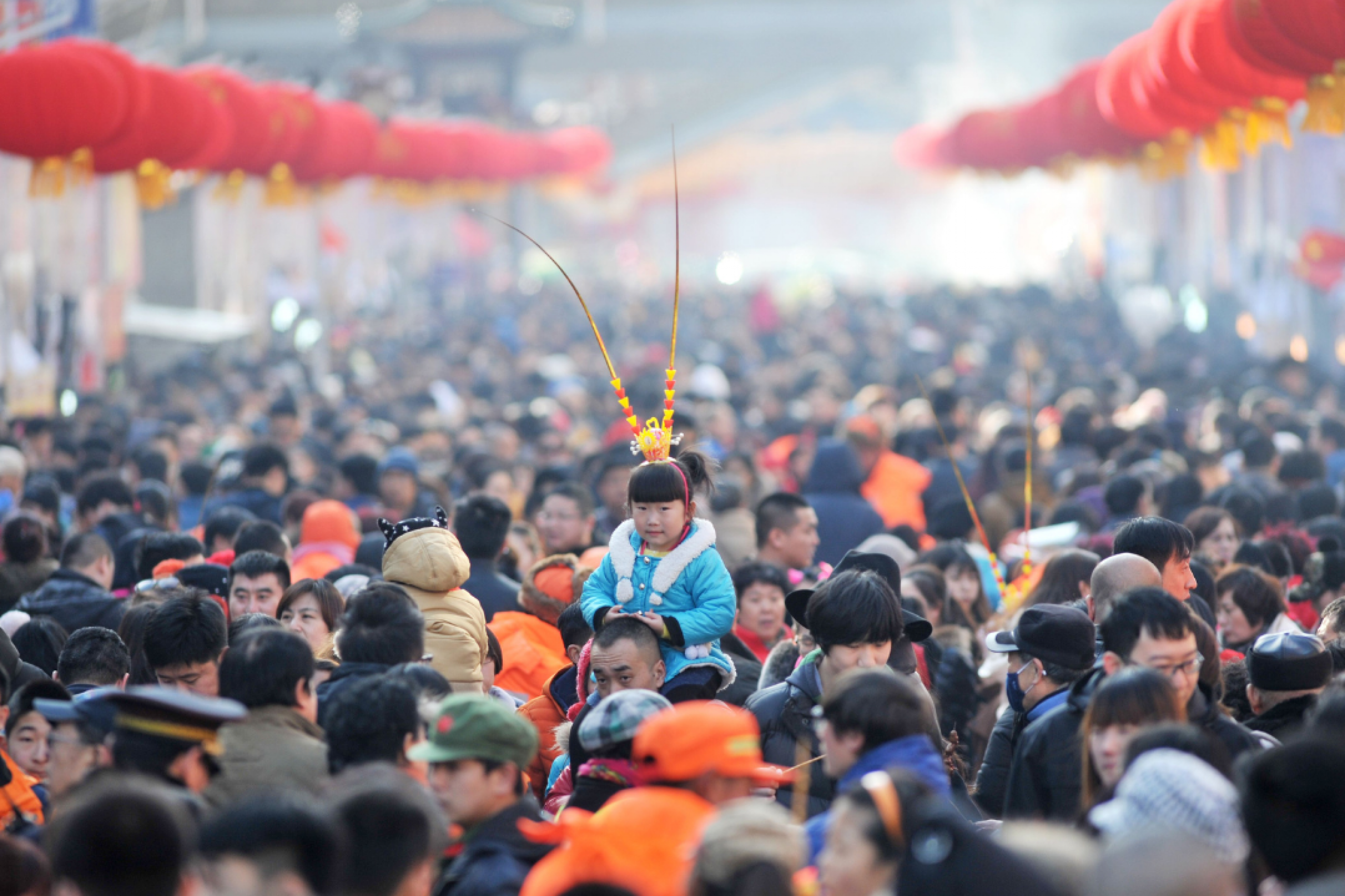 A girl wears a monkey king headwear as she sits on an adult's shouulders above a large crowd at a festival fair during Chinese Lunar New Year celebrations in Qingdao.