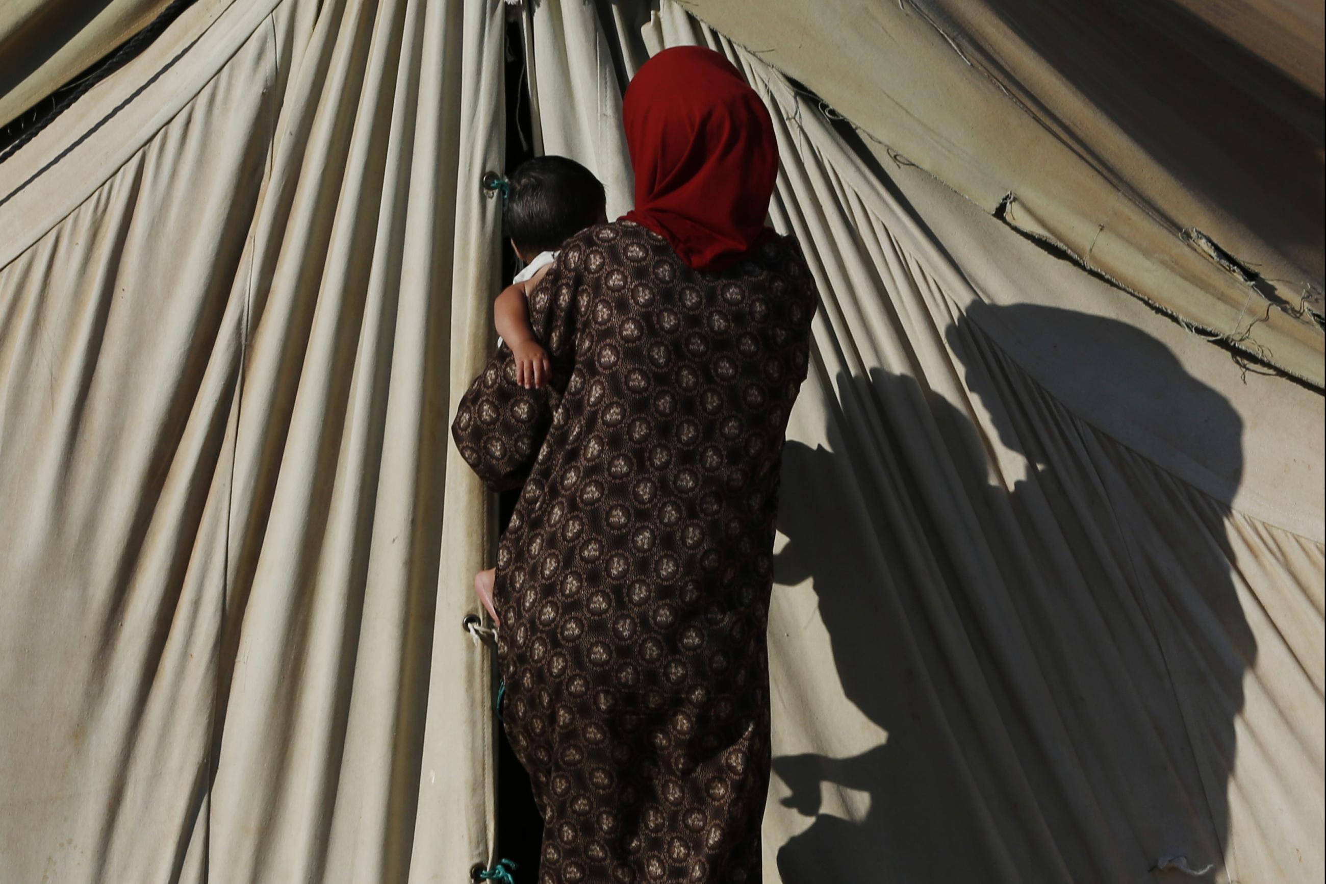 A Syrian refugee from Damascus, carries a child as she enters her tent, at the Majdal Anjar refugee camp in Bekaa Valley near the Syrian border in eastern Lebanon, on September 9, 2013.